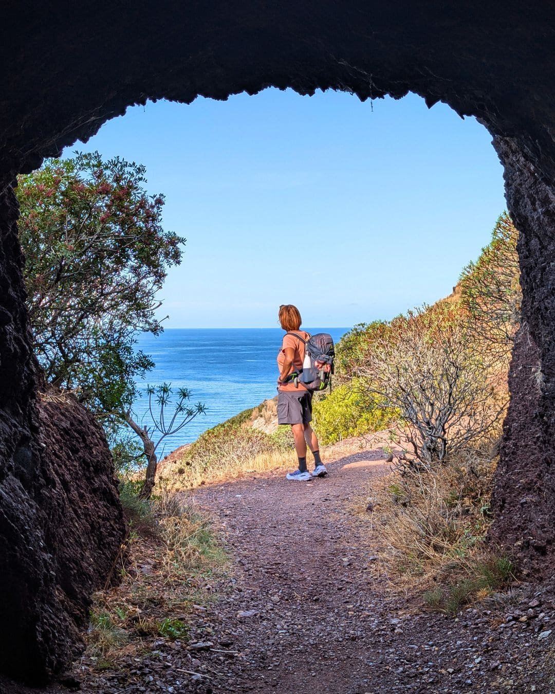 Ragazza con zaino che sorride davanti al mare della Sardegna sul Cammino Minerario di Santa Barbara