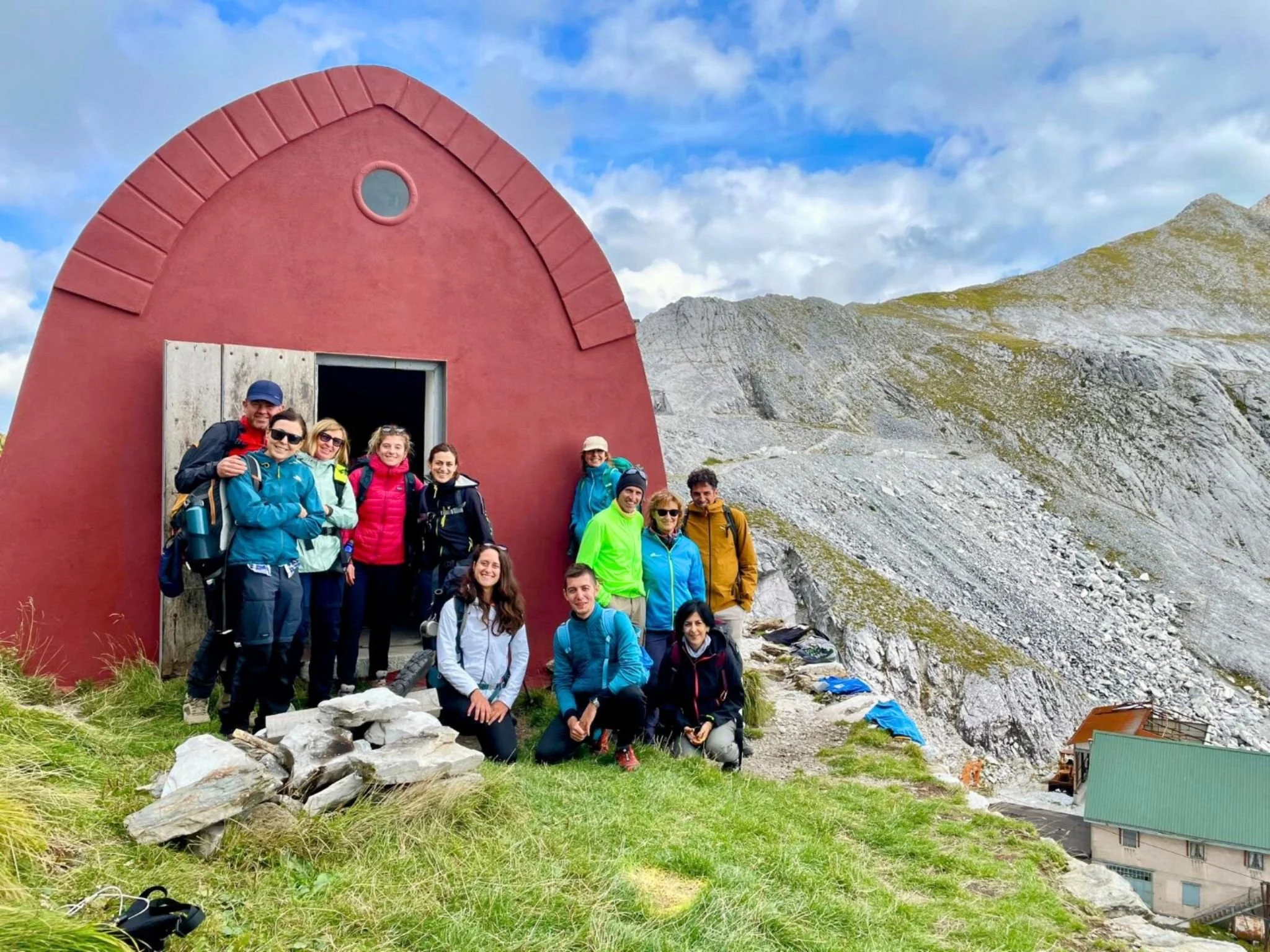 Escursionisti davanti a un bivacco durante un trekking nelle Alpi Apuane, con le montagne sullo sfondo