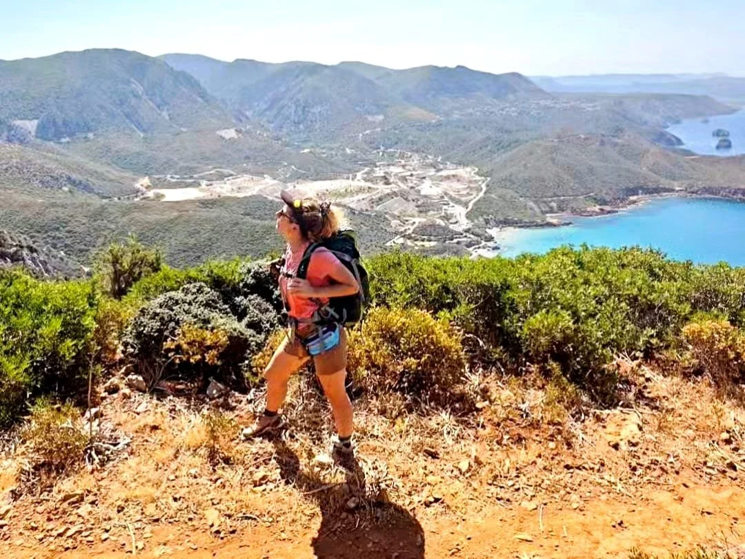 Ragazza escursionista sul Cammino Minerario di Santa Barbara in Sardegna, con vista sul mare e paesaggio costiero