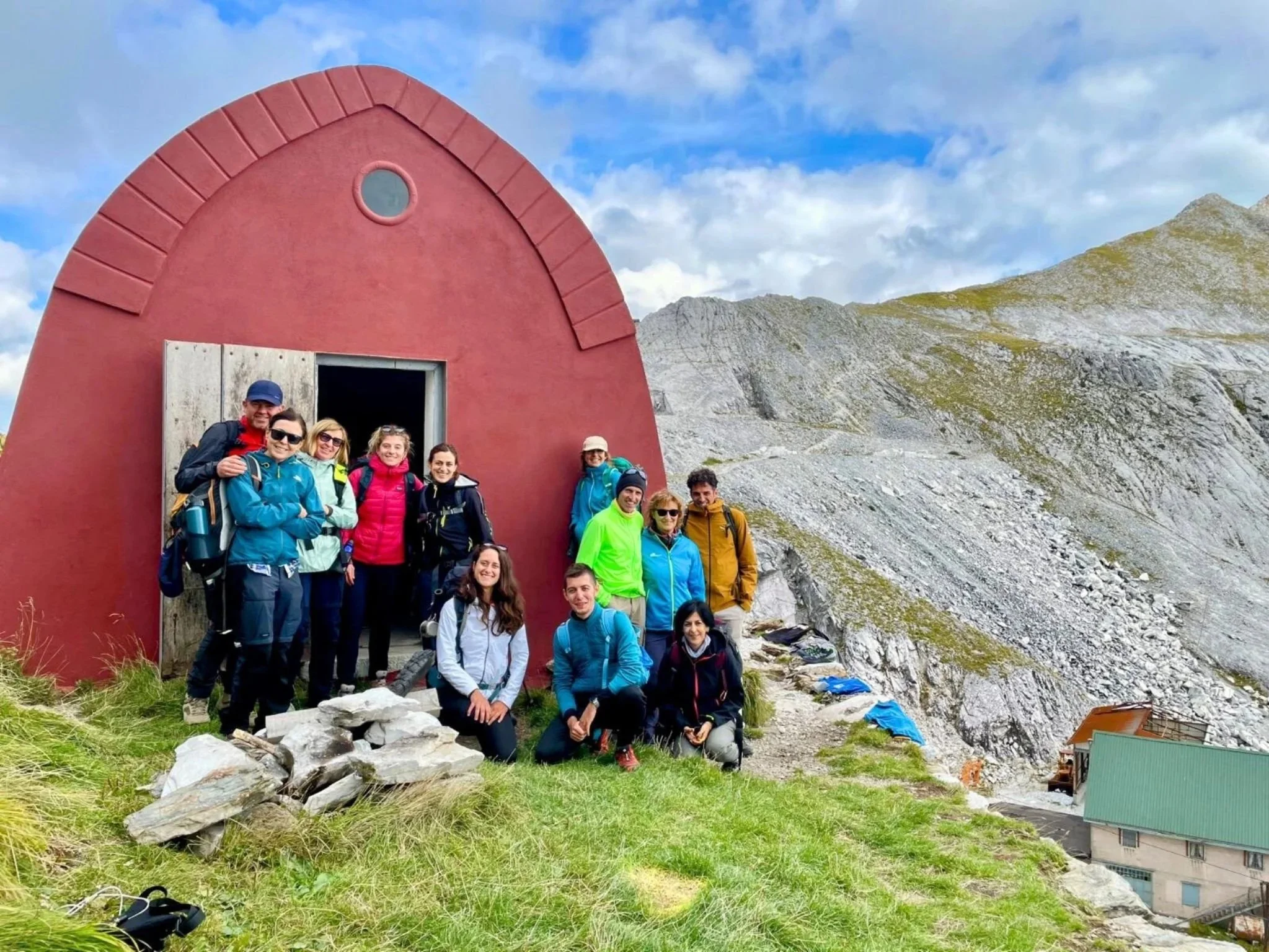 Escursionisti davanti a un bivacco durante un trekking nelle Alpi Apuane, con le montagne sullo sfondo