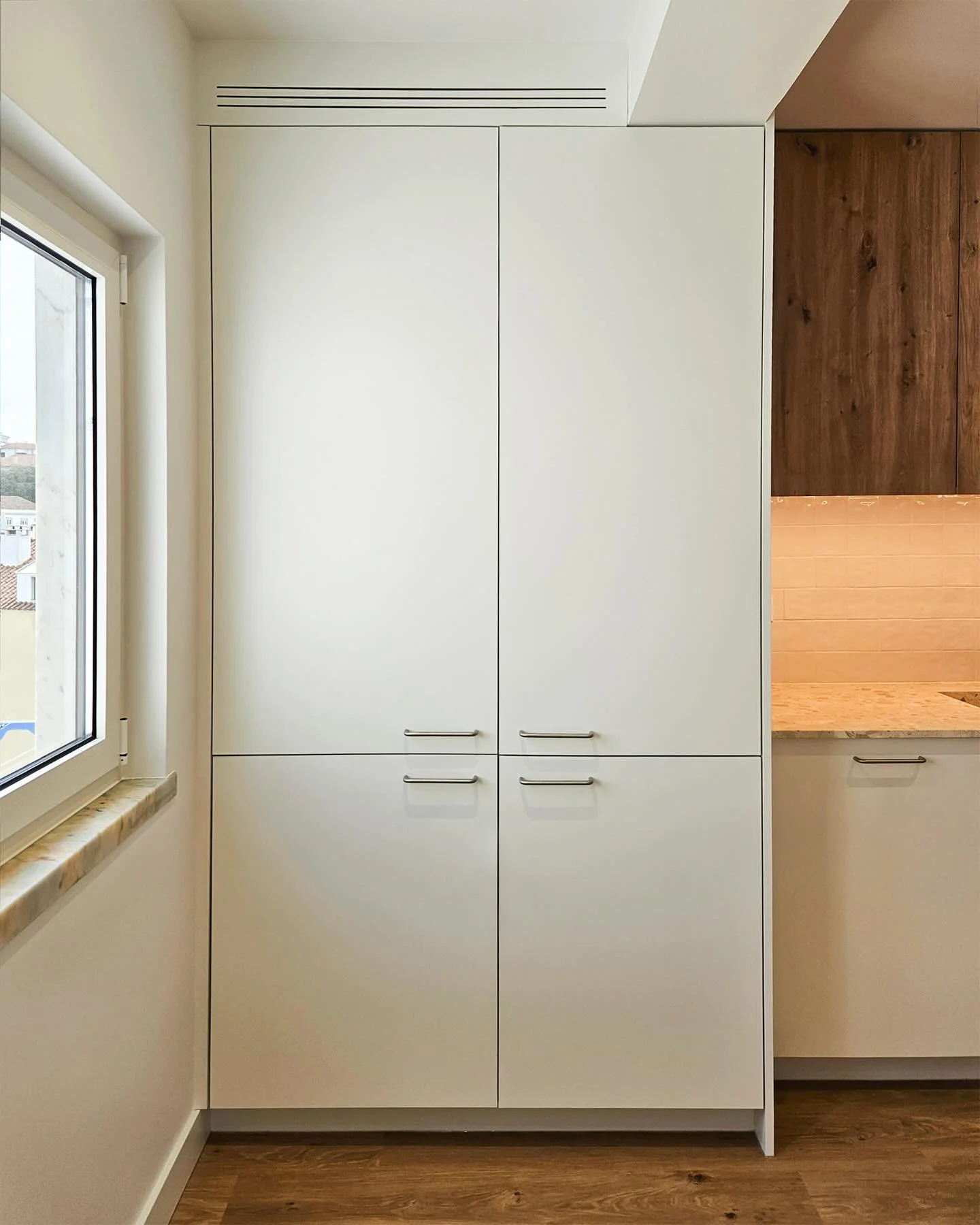 Clean lines, calm materials.

This unit combines white fronts with oak accents, designed as a fully integrated block. The fridge is hidden on the right, the washing machine discreetly integrated at the bottom left, with generous storage above. A subt