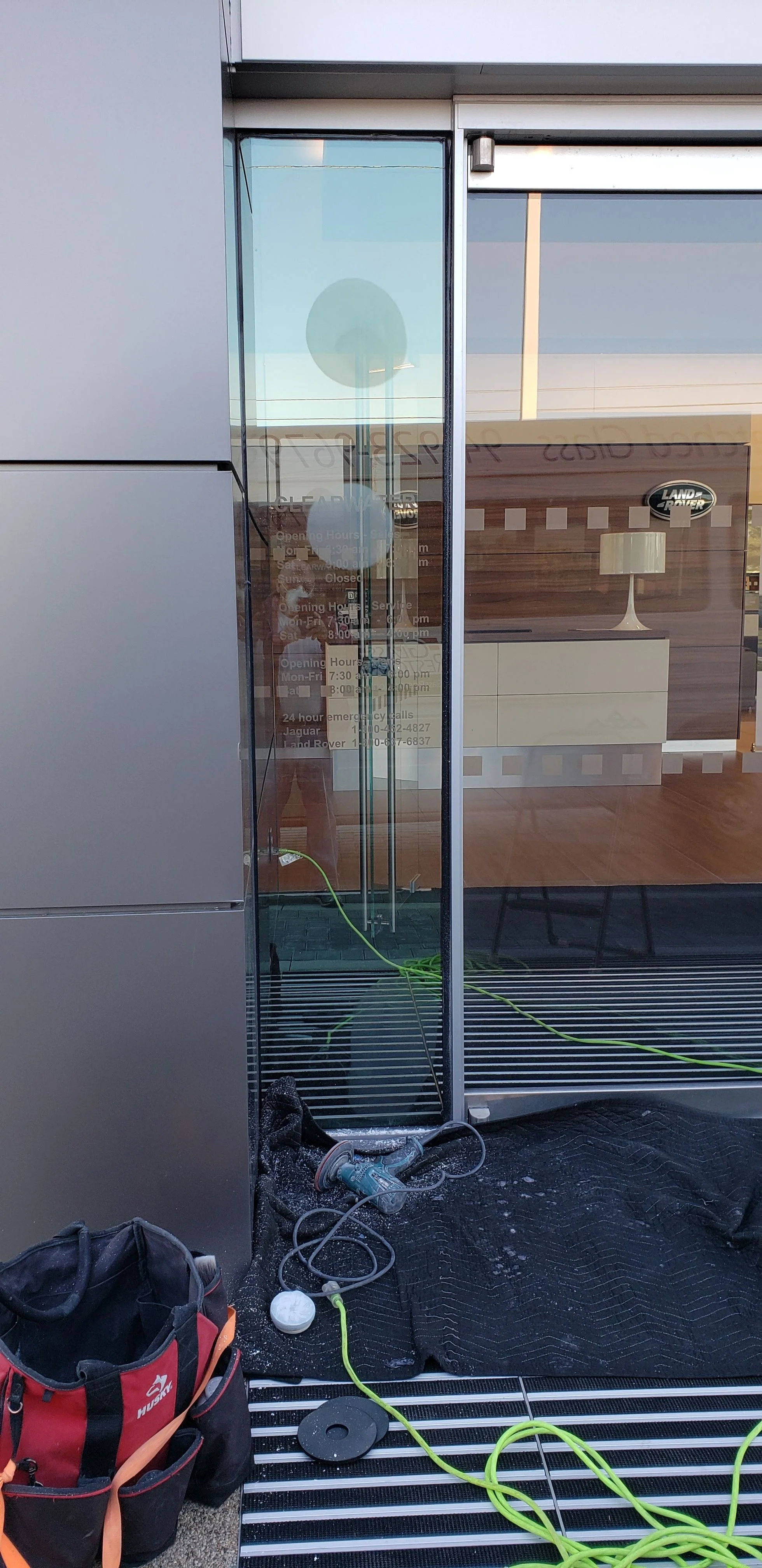 Glass Restoration Inc. technician working on the entry door glass at Jaguar of Clearwater — verified commercial storefront glass scratch repair at a luxury automotive dealership in Clearwater FL