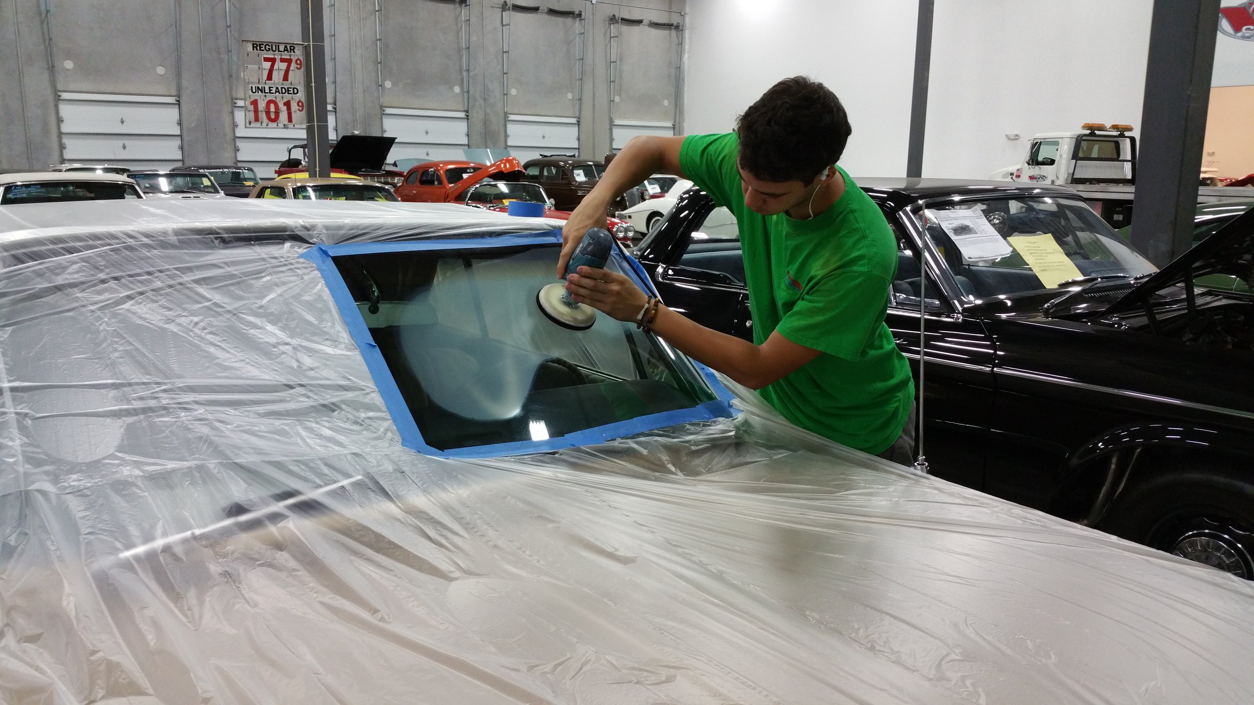 Person polishing a car windshield with a buffer in a garage setting.