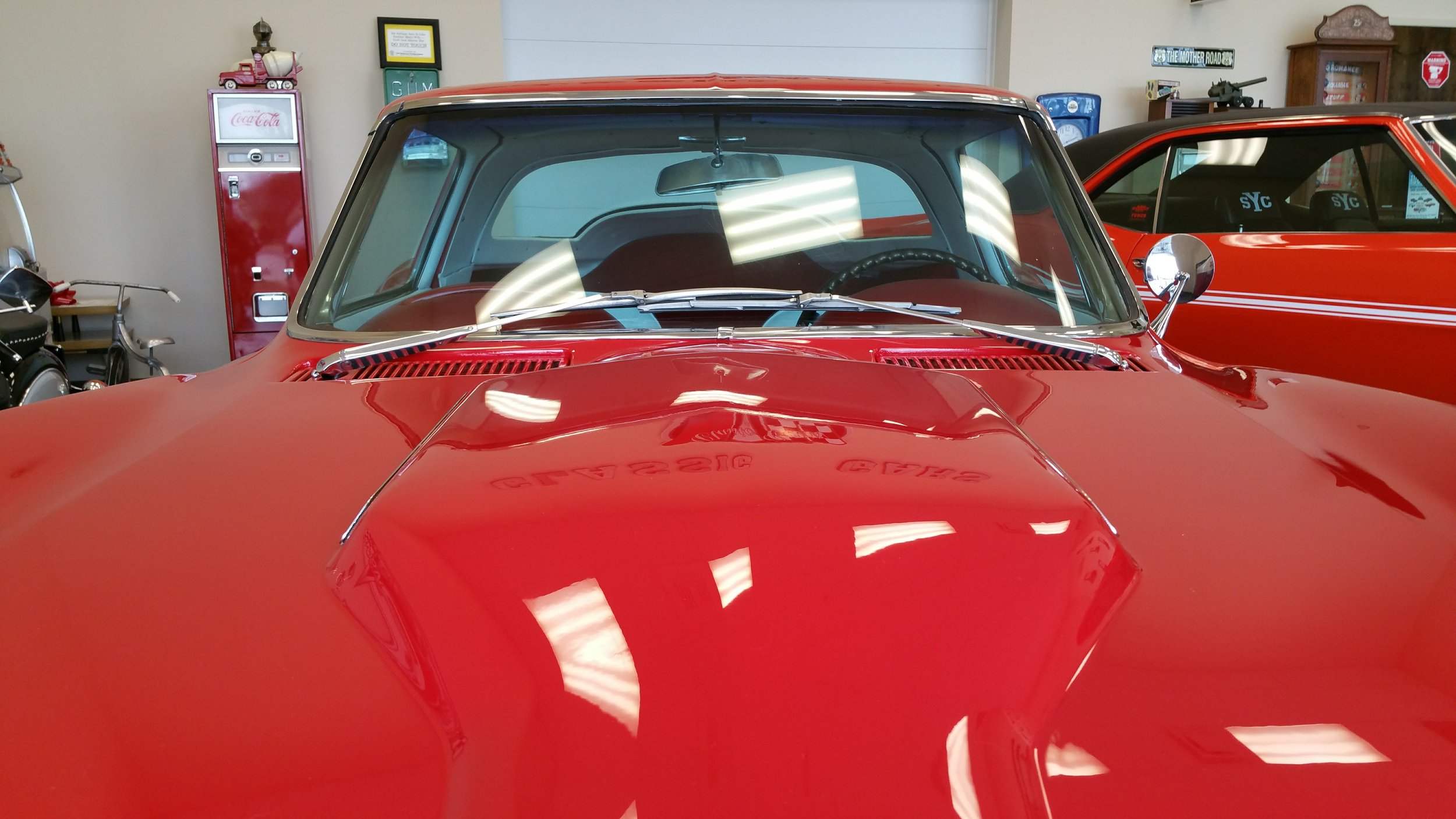 Front view of a red classic car inside a garage, with a vintage Coca-Cola vending machine in the background.