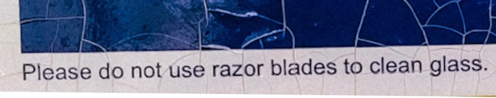 close-up, enlarged photograph of an official PGT window sticker, highlighting the specific manufacturer's warning text: 'NOTICE: DO NOT USE razor blades to clean glass' to prevent permanent scratching.
