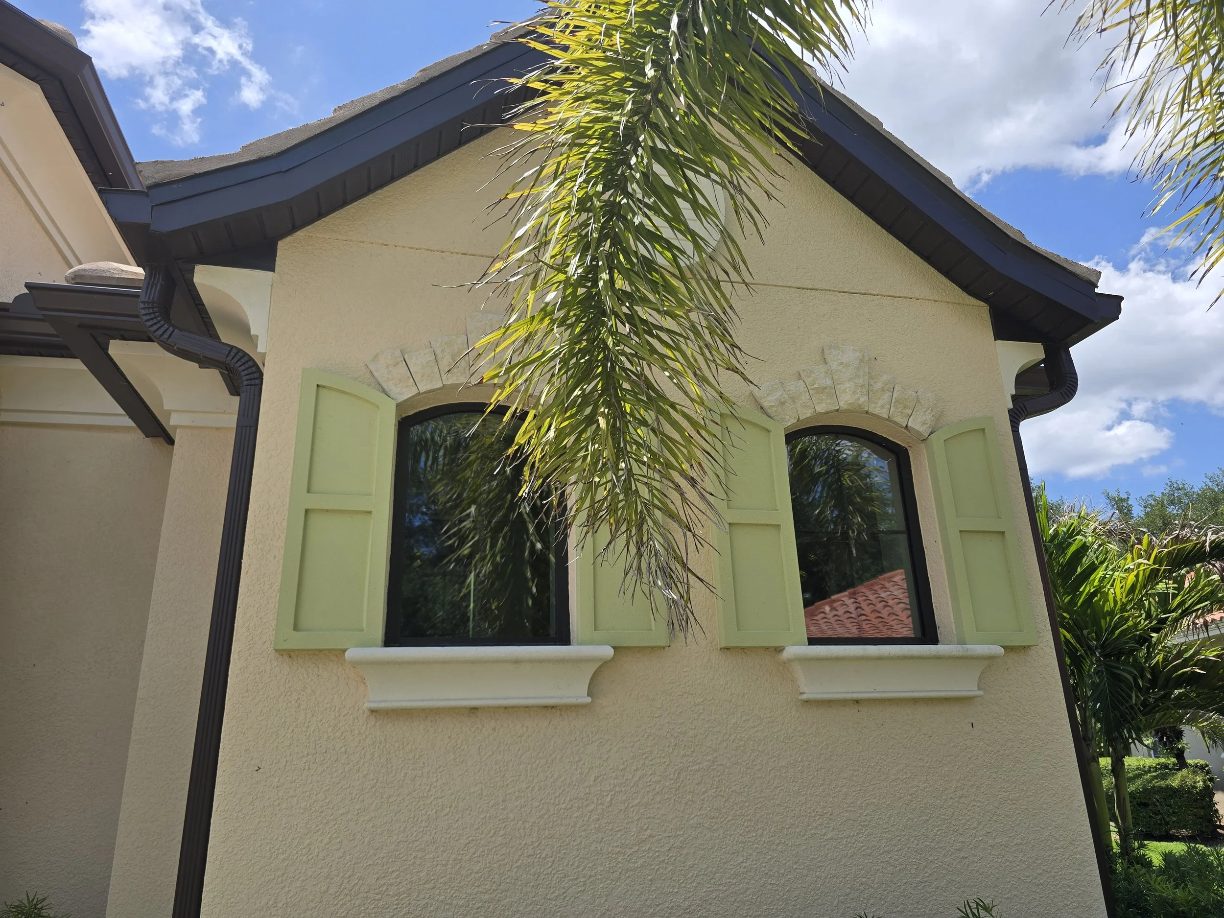 Restored arch top and oval impact-rated fixed windows on the front elevation of a Founders Club home in Sarasota FL — three windows total, restored on-site by Glass Restoration Inc.