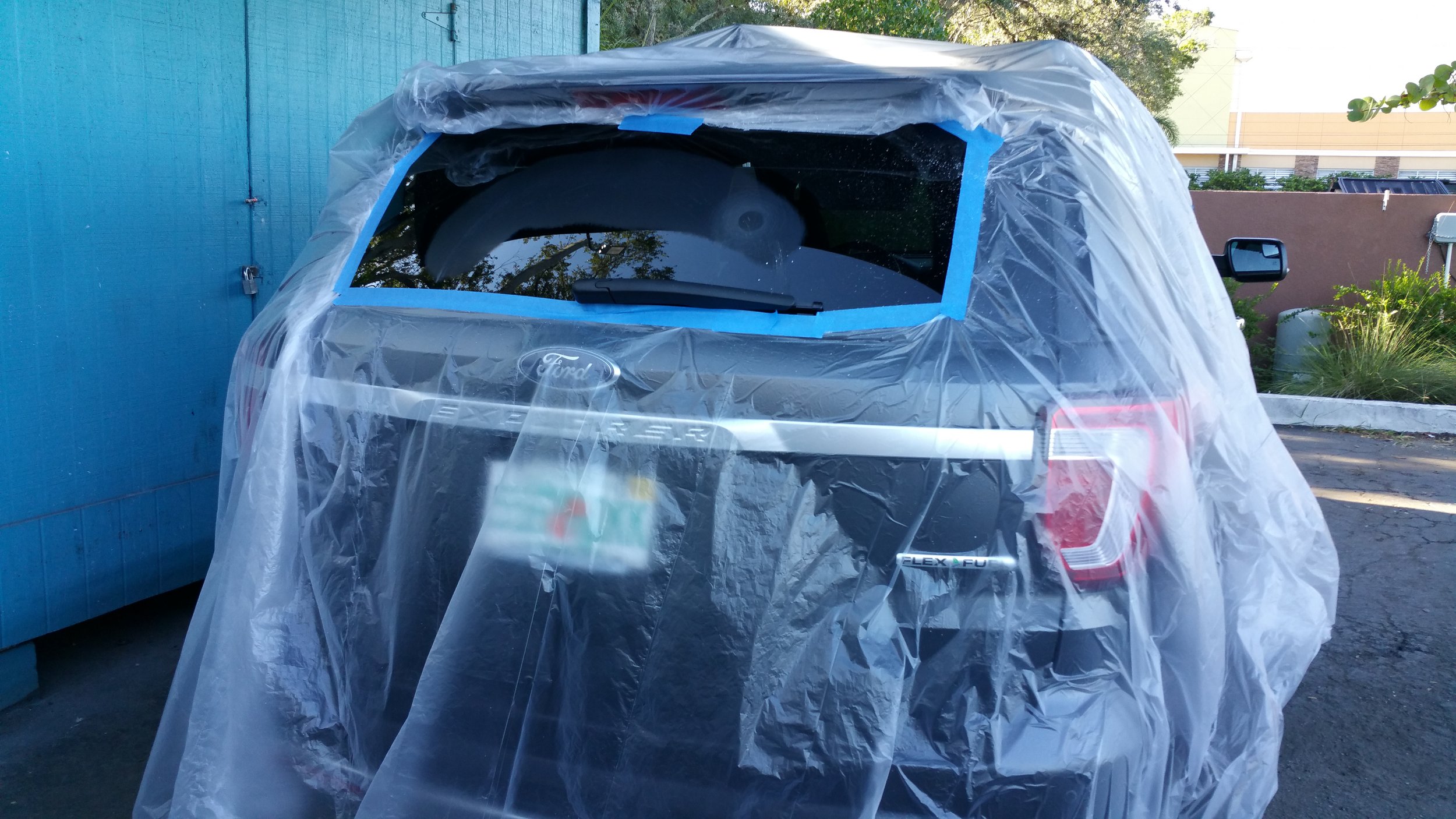 A black Ford Explorer with its rear covered in protective plastic and masking tape, parked outdoors. Wiper scratches being fixed
