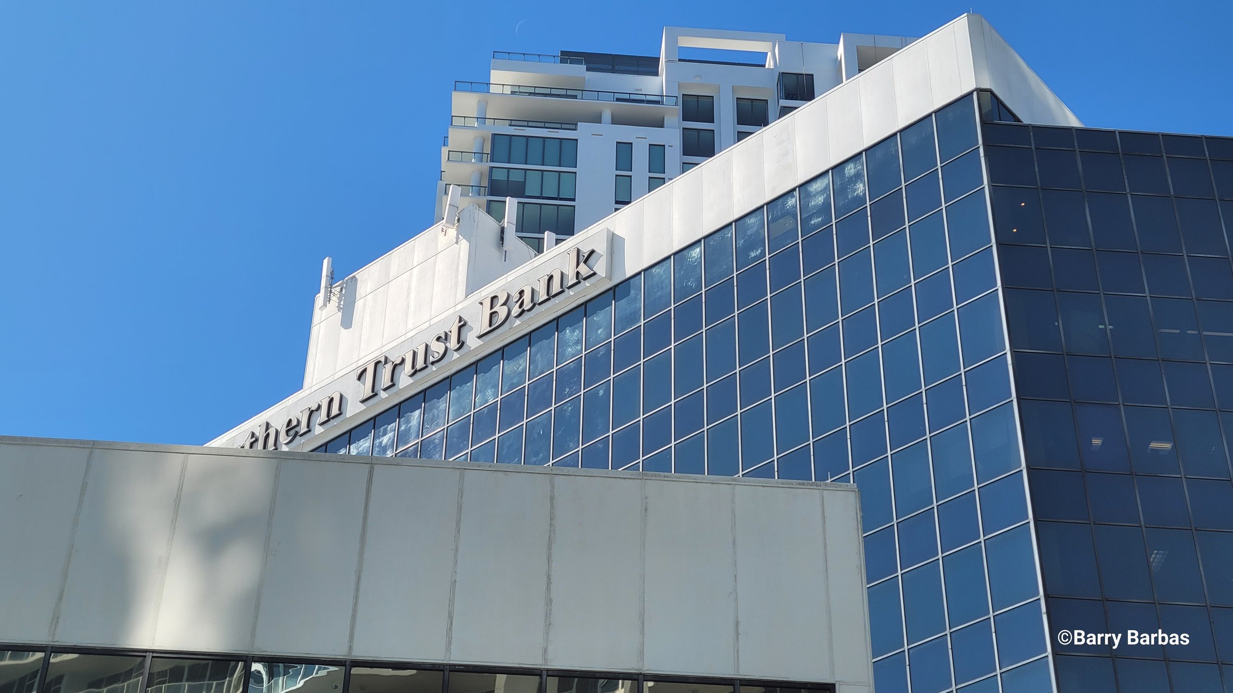 Partial view of Northern Trust Bank building with modern glass and concrete architecture against a clear blue sky.