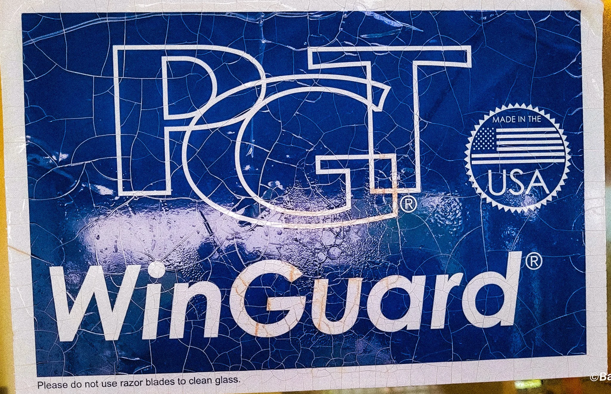 A close-up, enlarged photograph of an official PGT window sticker, highlighting the specific manufacturer's warning text: 'NOTICE: DO NOT USE razor blades to clean glass' to prevent permanent scratching
