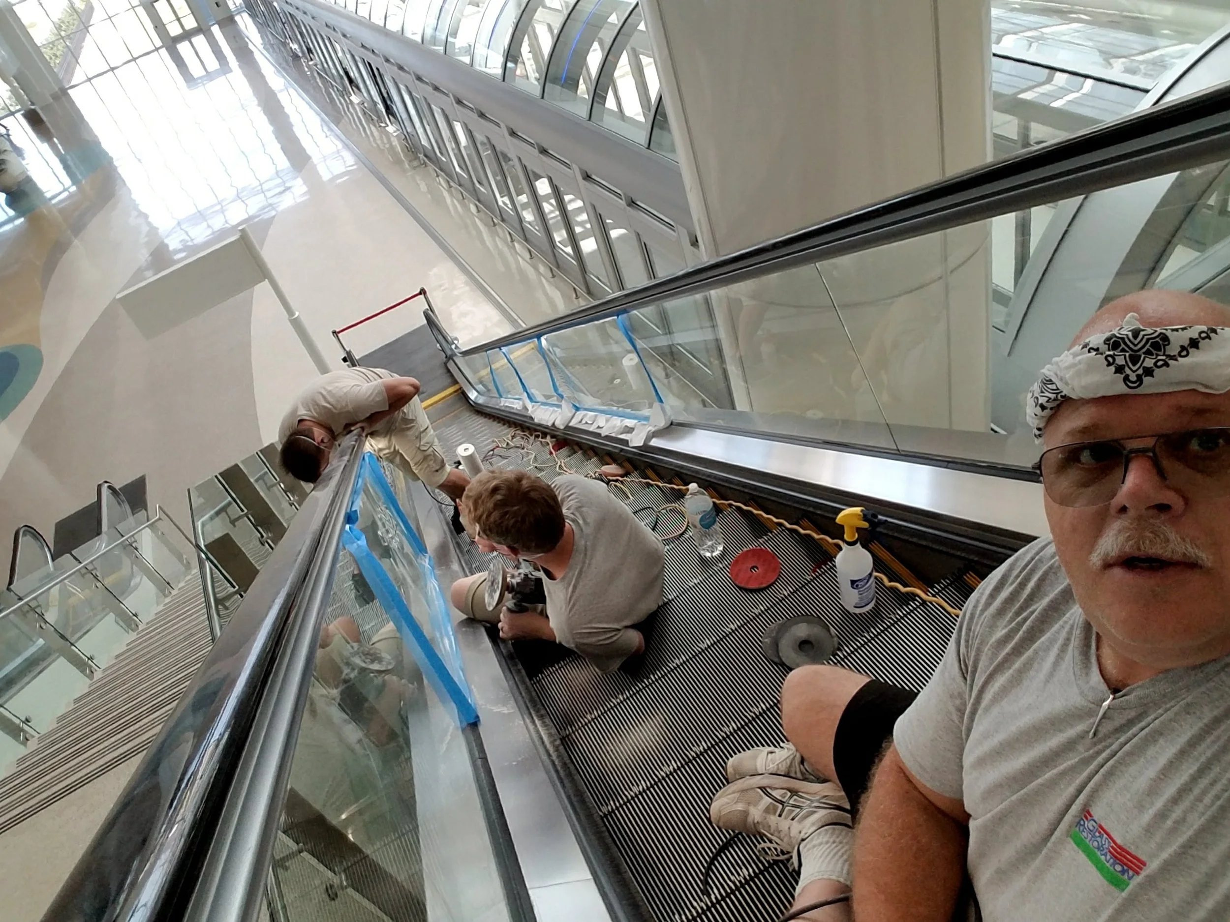 Barry Barbas, Skyeler Schmidt, and Stanton Barbas of Glass Restoration Inc. performing on-site scratch repair on escalator glass at an airport facility