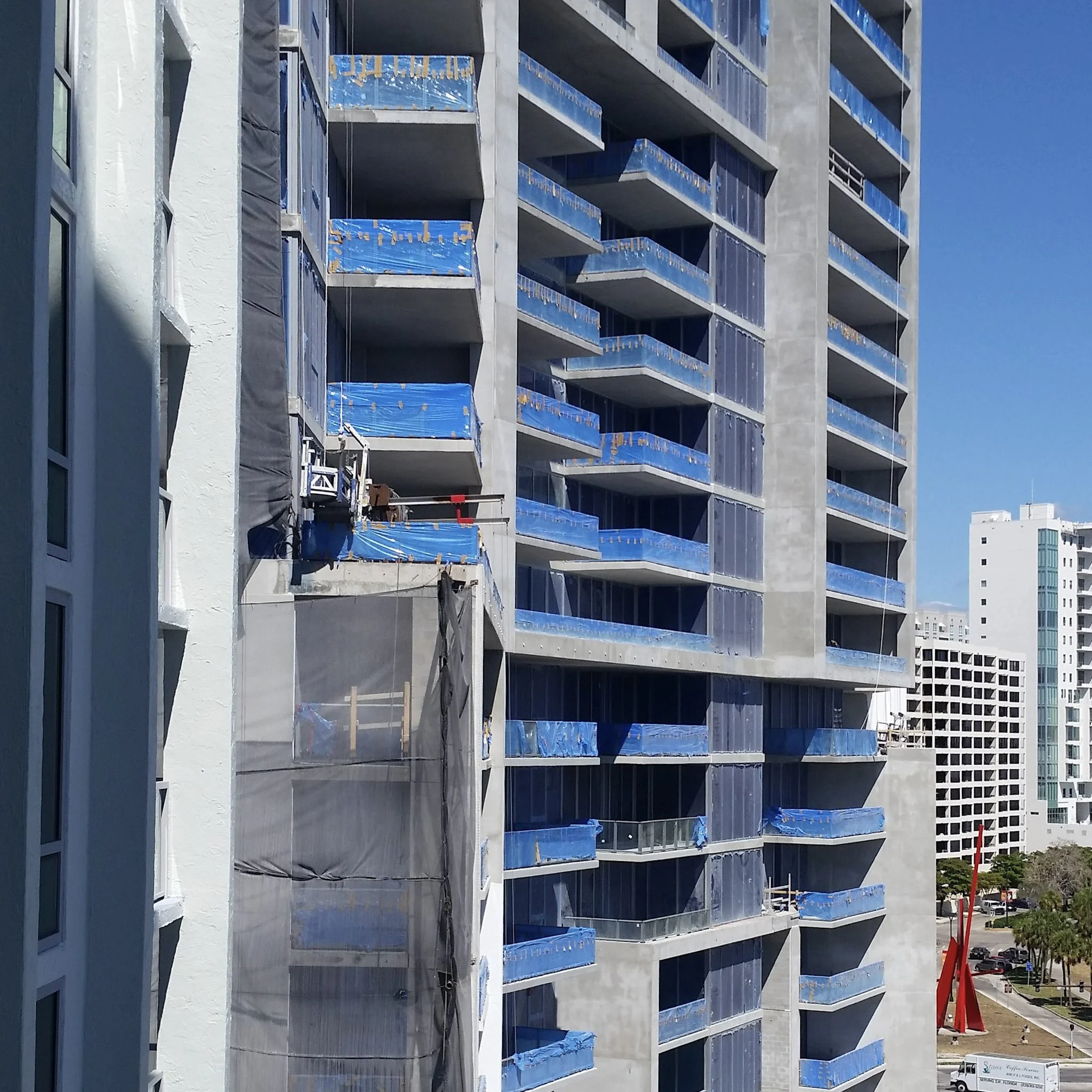 Blue protective construction film left on glass railings of a downtown Sarasota high-rise — a common sight on Florida Gulf Coast construction projects where manufacturer removal timelines are not followed
