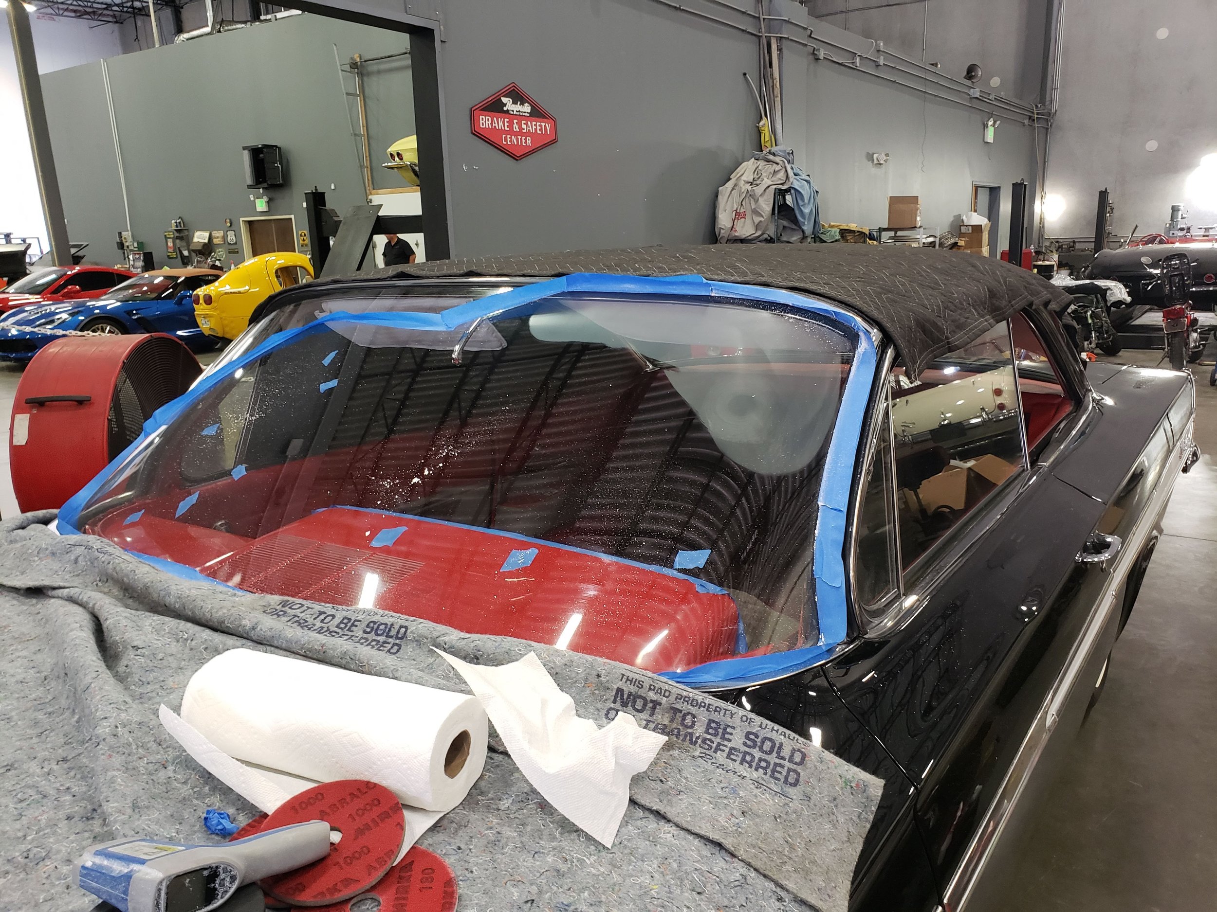 Classic car in a garage with taped windshield and repair tools nearby.