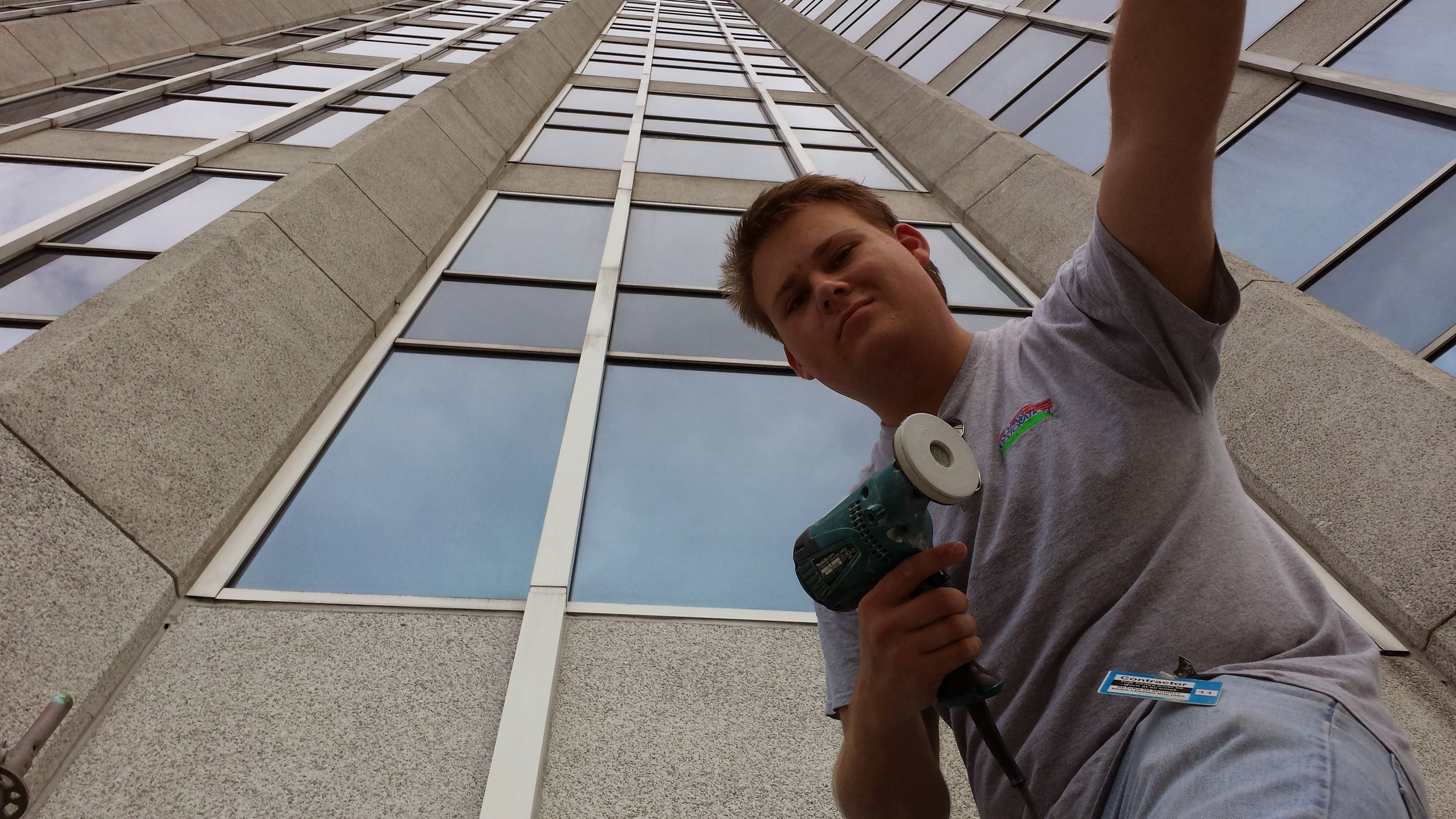 Person holding a power drill in front of a tall building, looking up.
