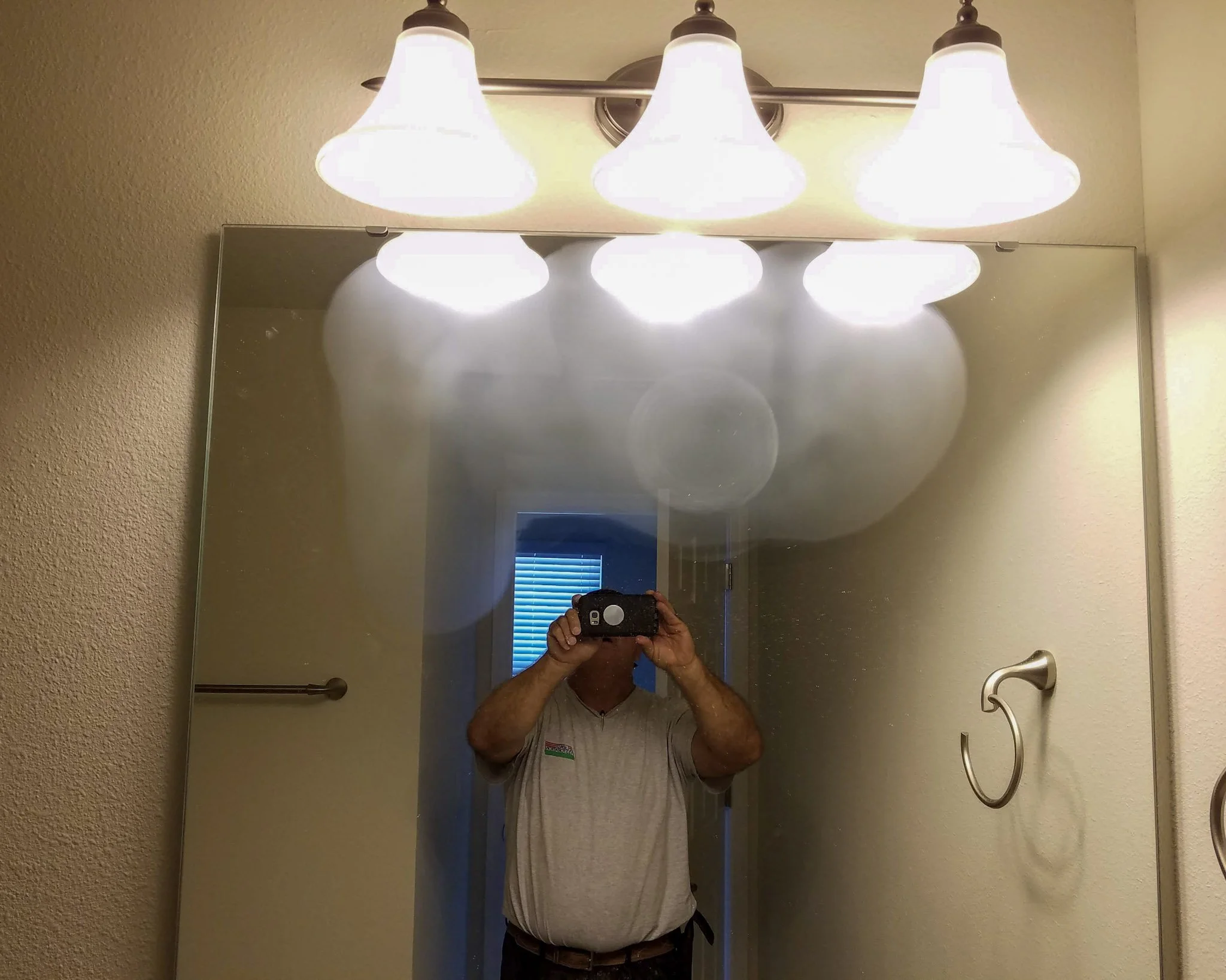 Glass Restoration Inc. technician restoring a large area of scratched mirror glass under a vanity light — professional on-site mirror resurfacing serving Florida homeowners with honest assessment and disclosed breakage risk before every job
