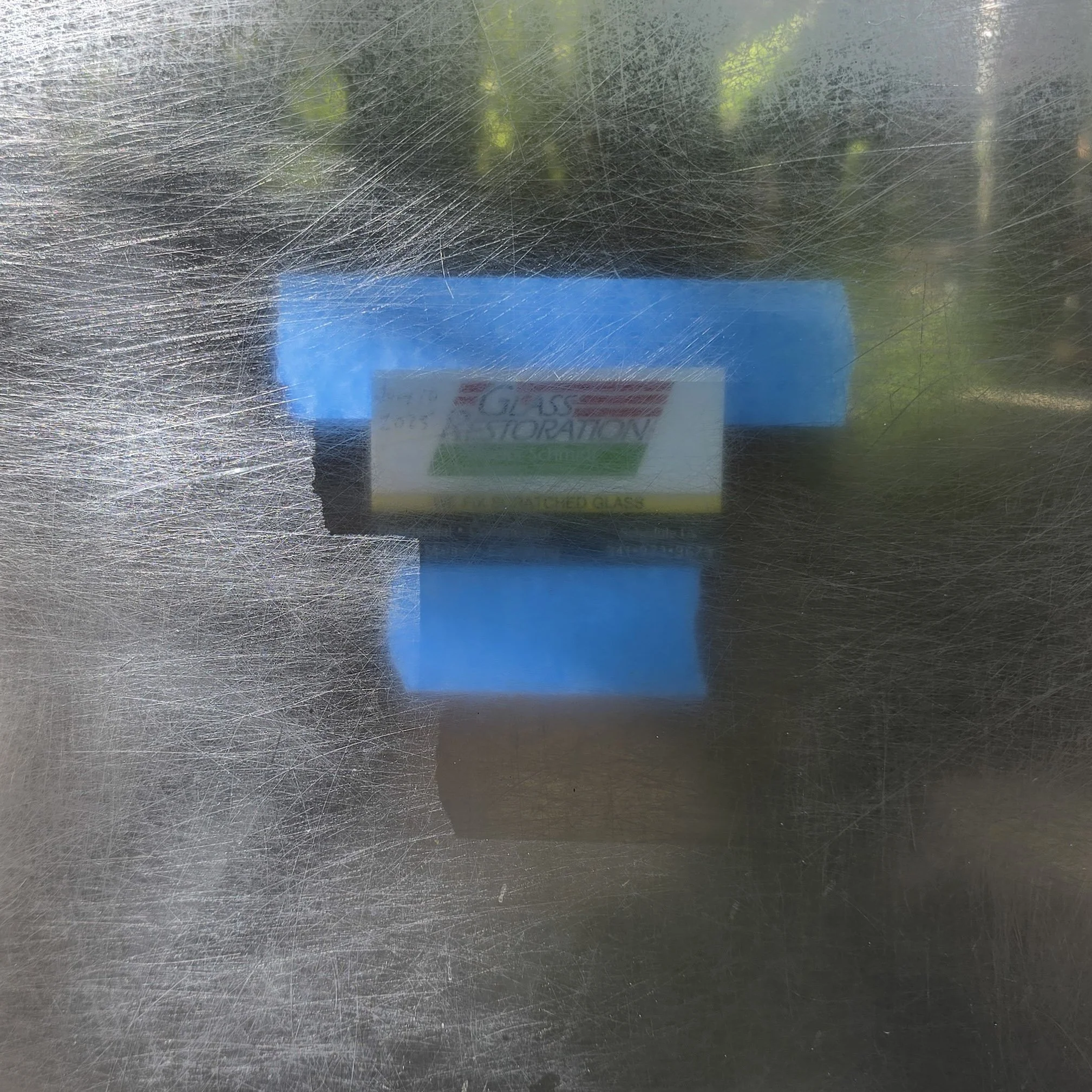 Scratched and foggy glass surface with a blurred background and partial view of a blue and white box with text.