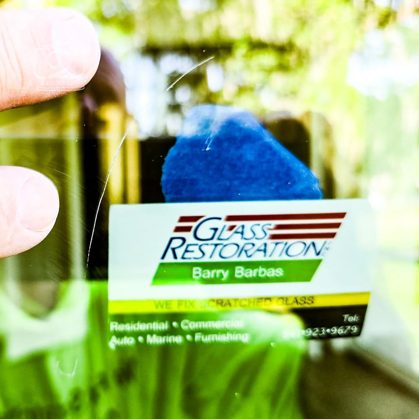 Glass Restoration Inc. business card taped to glass as a focal point beside a scratch — diagnostic technique used on Hernando County FL glass restoration jobs to photograph and assess damage accurately