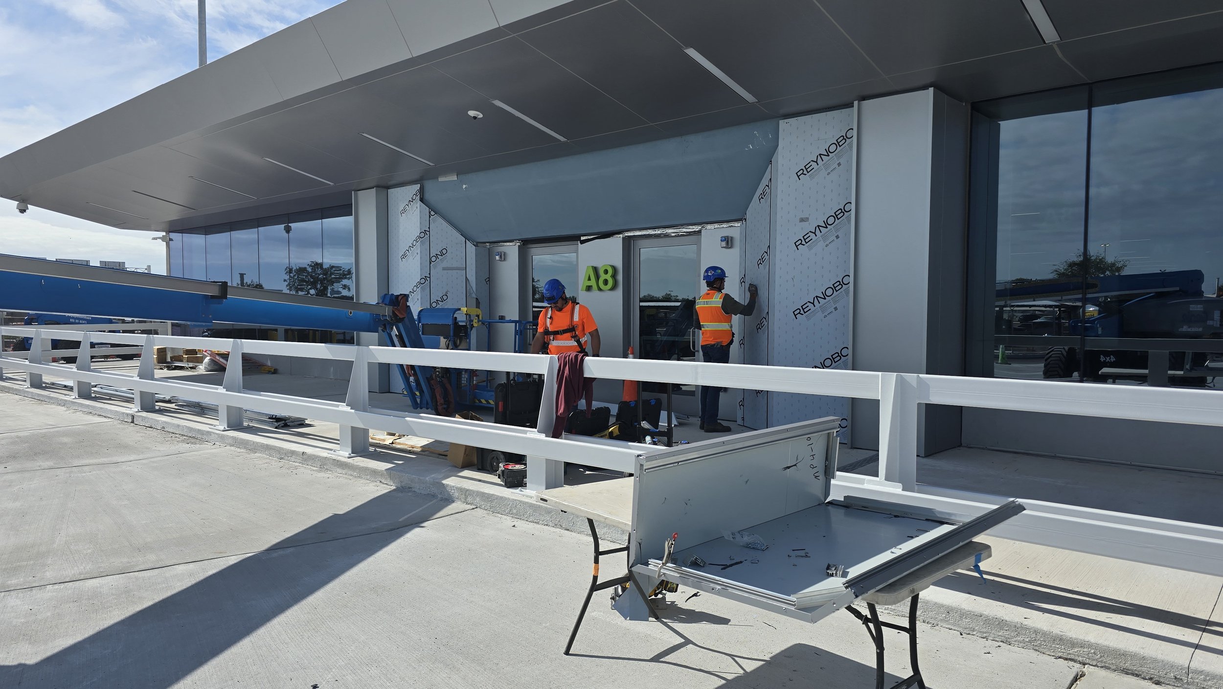 Construction workers in safety gear working on a building entrance labeled A8, with equipment and materials on site.