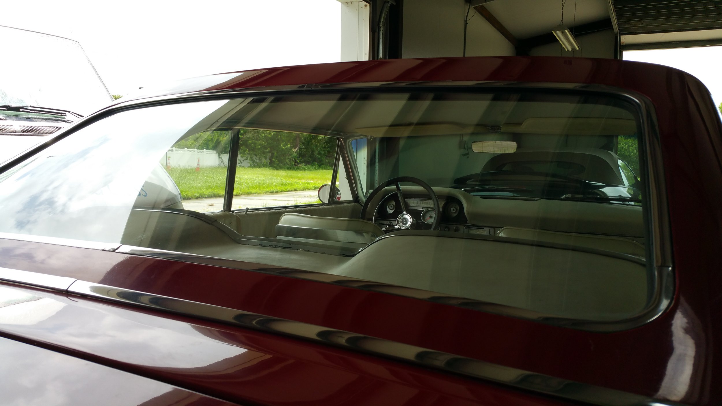 Interior of a classic vintage car with a view through the rear window, showcasing the steering wheel and dashboard.