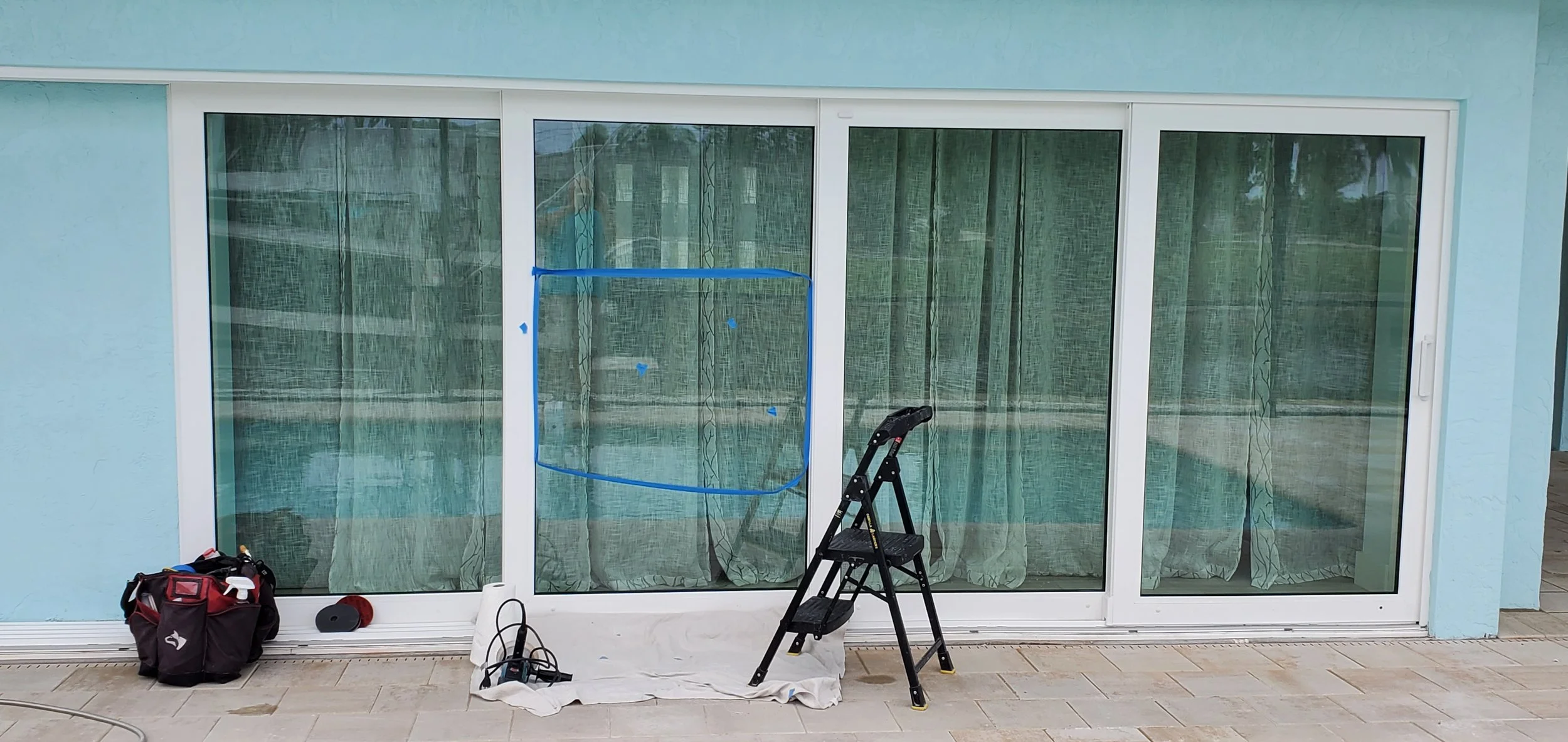 Glass Restoration Inc. technician setup at a four panel sliding glass door in Timber Pines Spring Hill FL — drop cloth, work stool, and tool bag in position for professional on-site glass scratch repair and hard water stain removal