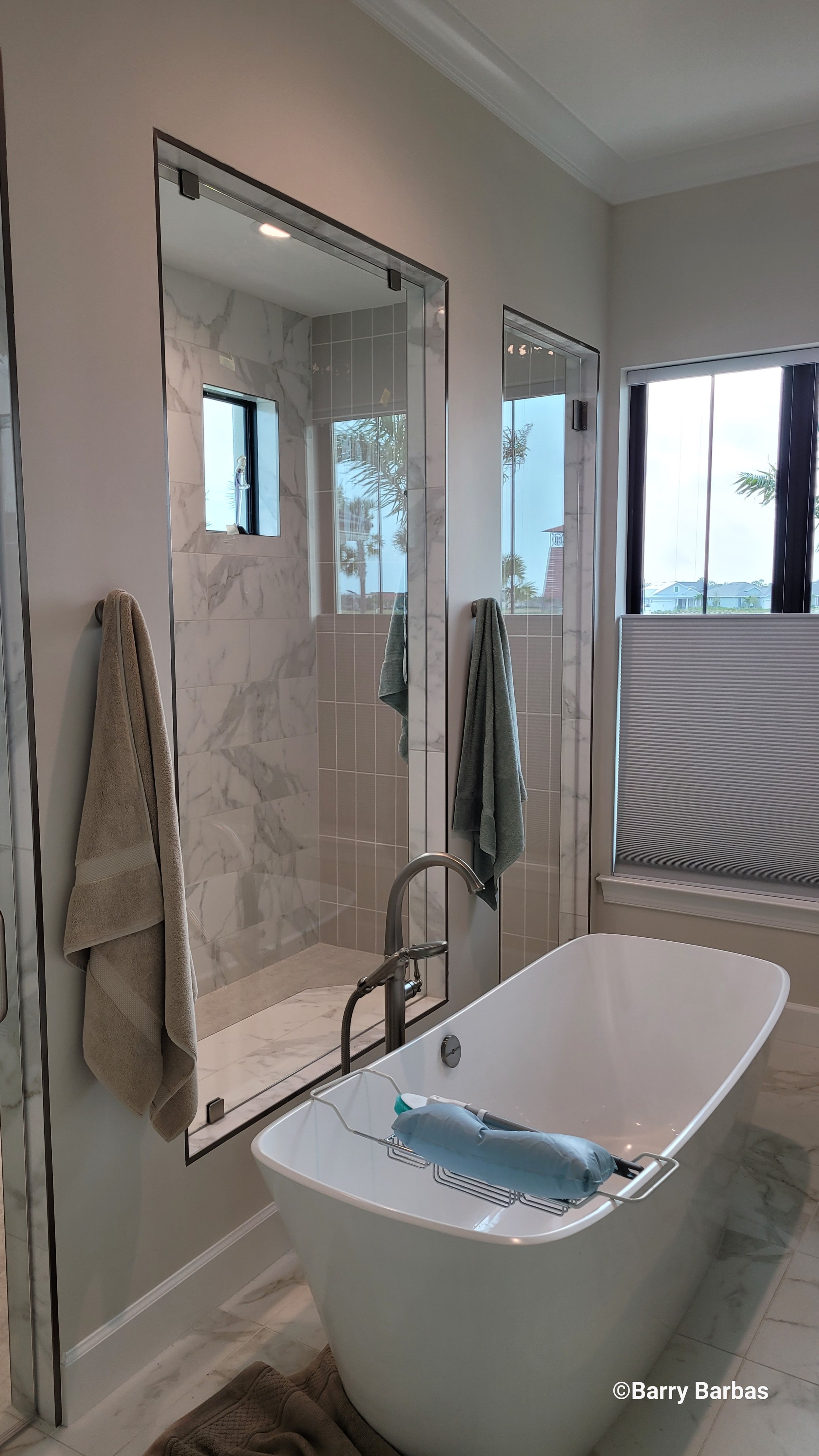 Modern bathroom with a freestanding bathtub, marble tiles, walk-in shower, and towels hanging on racks. A small window lets in natural light.