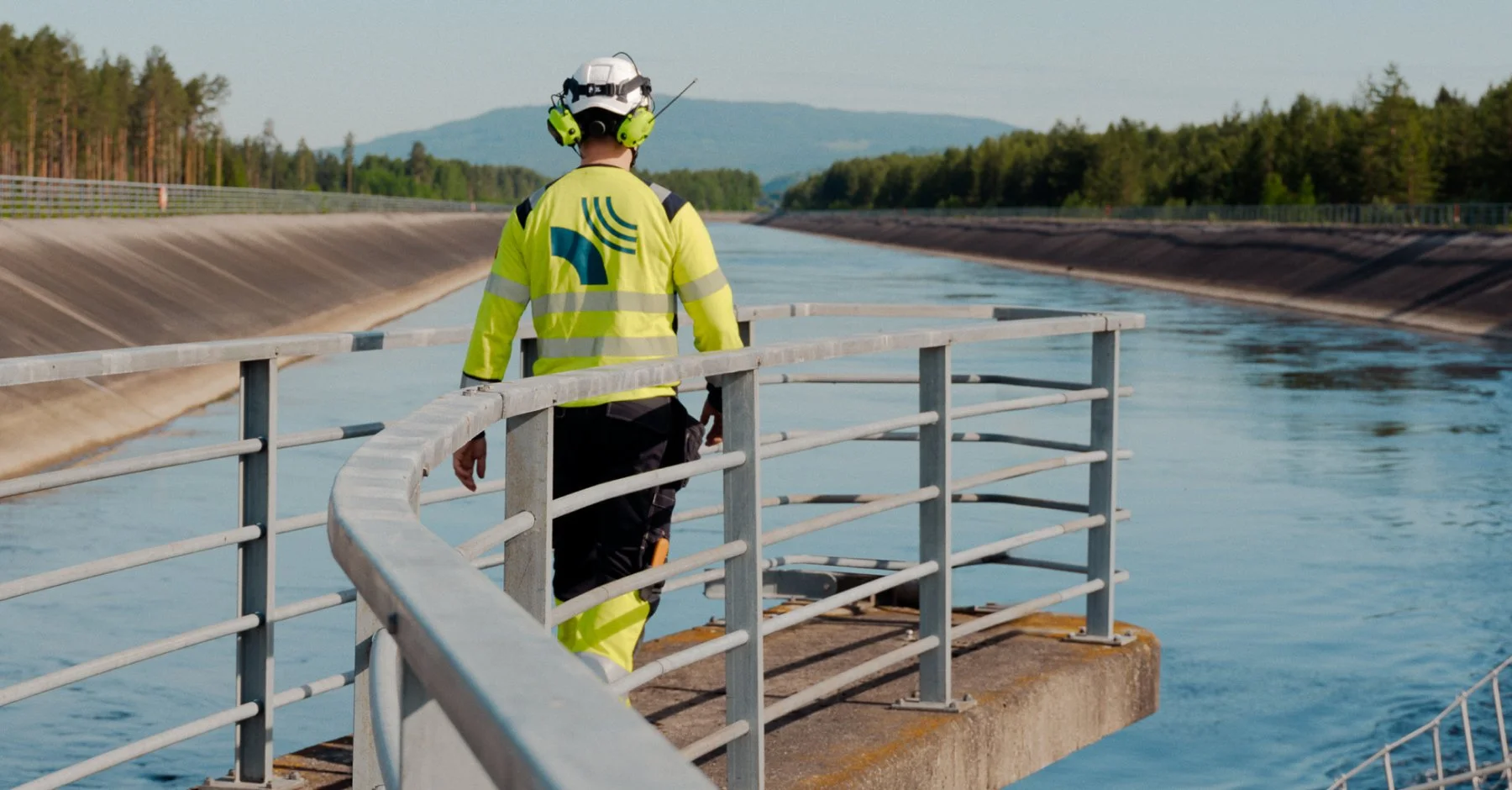 En person i høyvis med hørselsvern og refleksvest går langs en vannkilde omringet av et gjerde.
