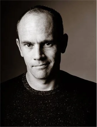 Black and white portrait of a man with a receding hairline, short hair, and a slight smile, wearing a dark sweater.