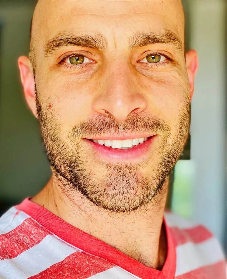 Close-up of a smiling man with a beard, wearing a red and white striped shirt.