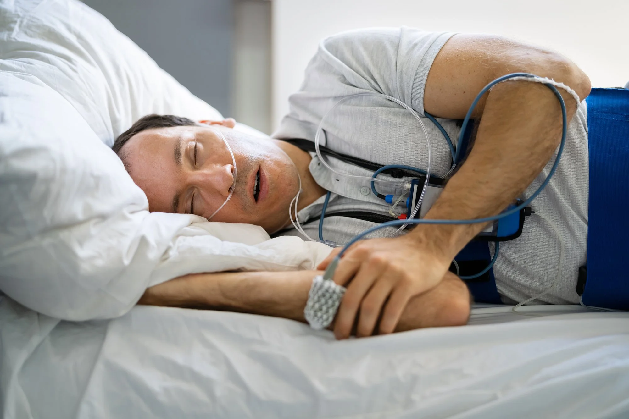 A man sleeping in a hospital bed with medical monitoring devices attached.