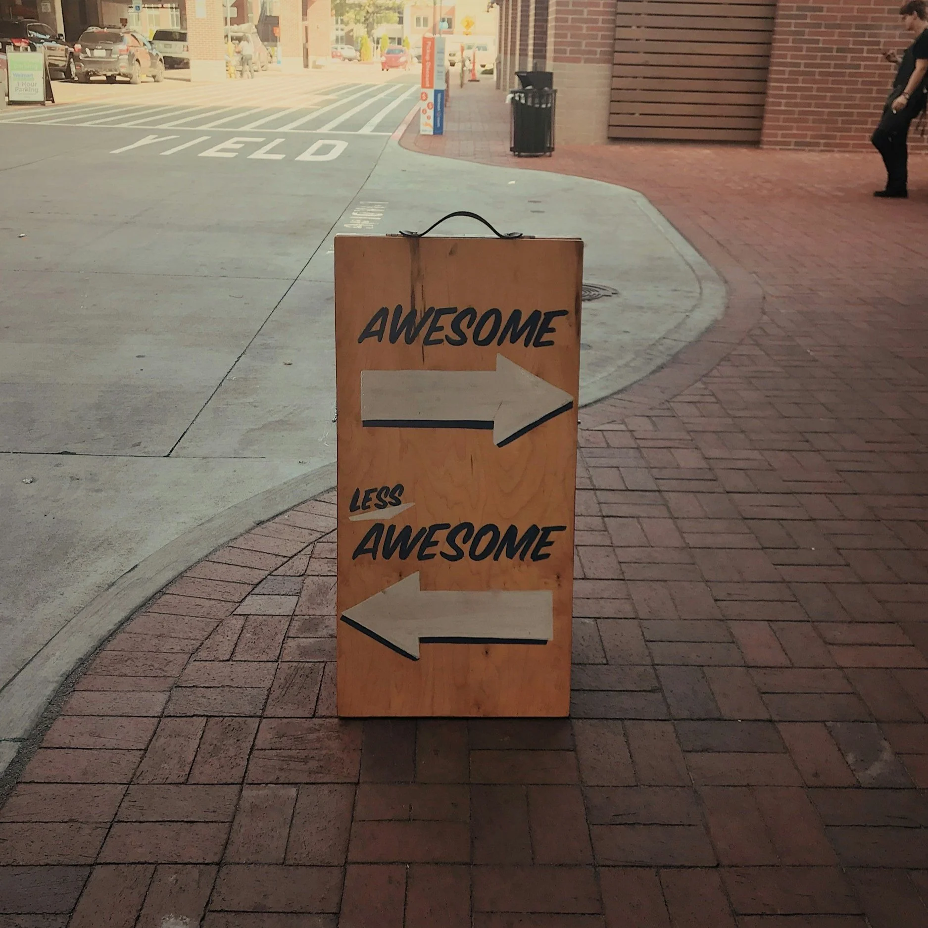 Wooden sign with two arrows. The top arrow pointing to the right labeled 'AWESOME,' and the bottom arrow pointing to the left labeled 'LESS AWESOME.'