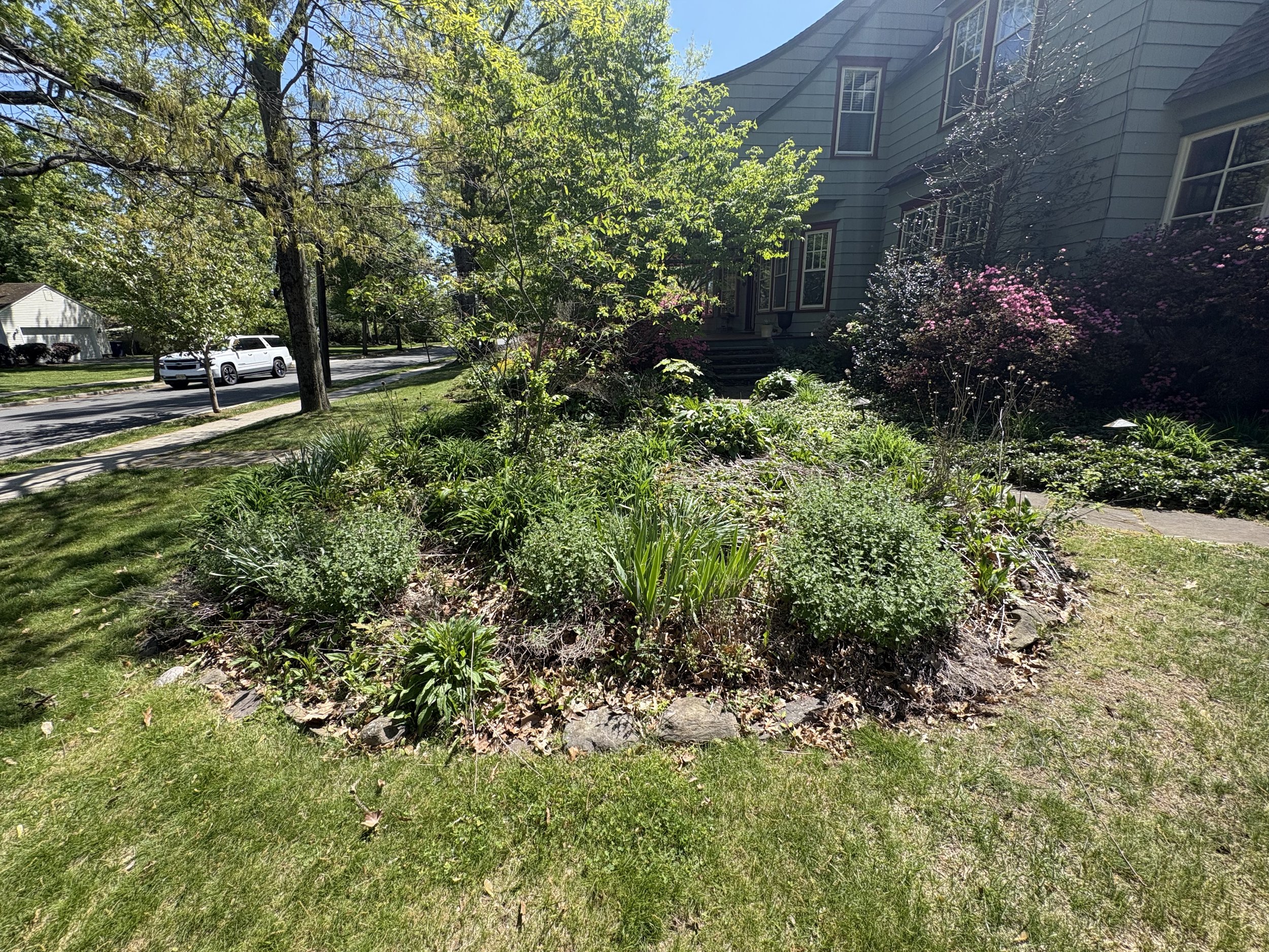 Backyard patio area with stone staircase leading to upper deck, black mulch garden beds, a small brick pillar, and various construction materials.
