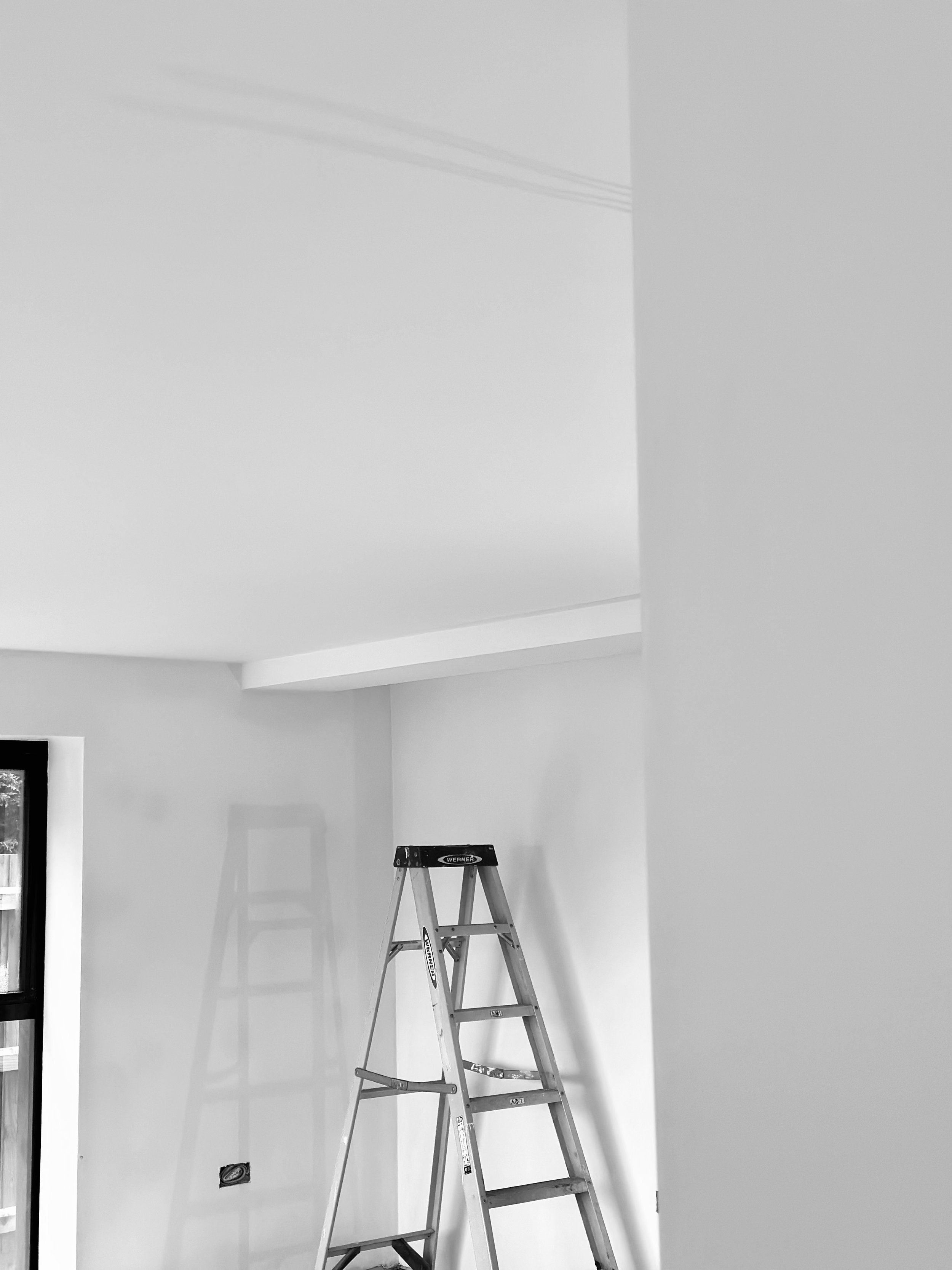 Black and white image of an empty room with a ladder and window.