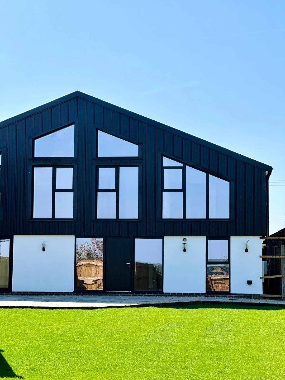 Modern two-story house with black exterior, large windows, green lawn, and clear blue sky.