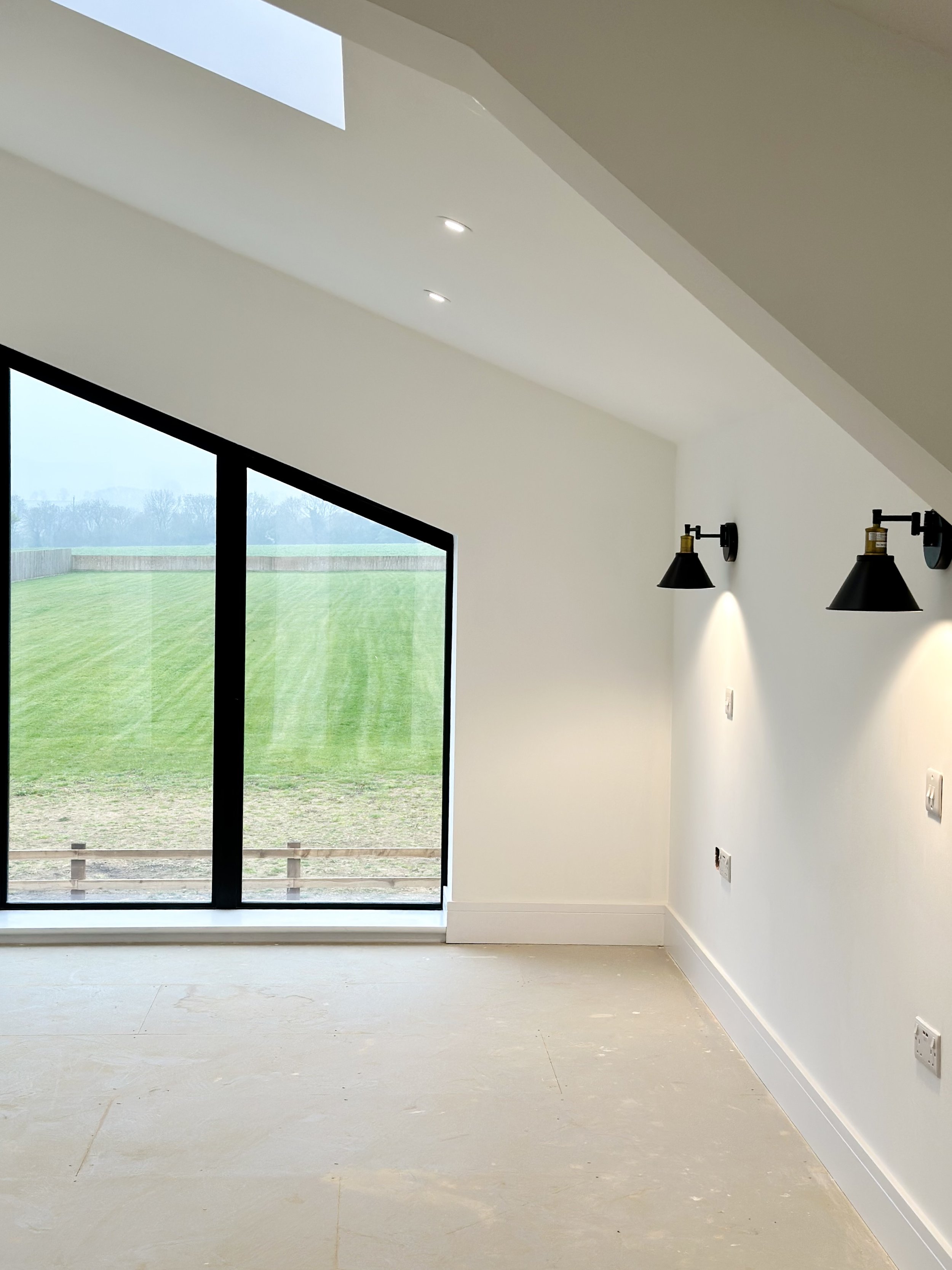 Minimalist room with large window, angled ceiling, sconces, and view of grassy field