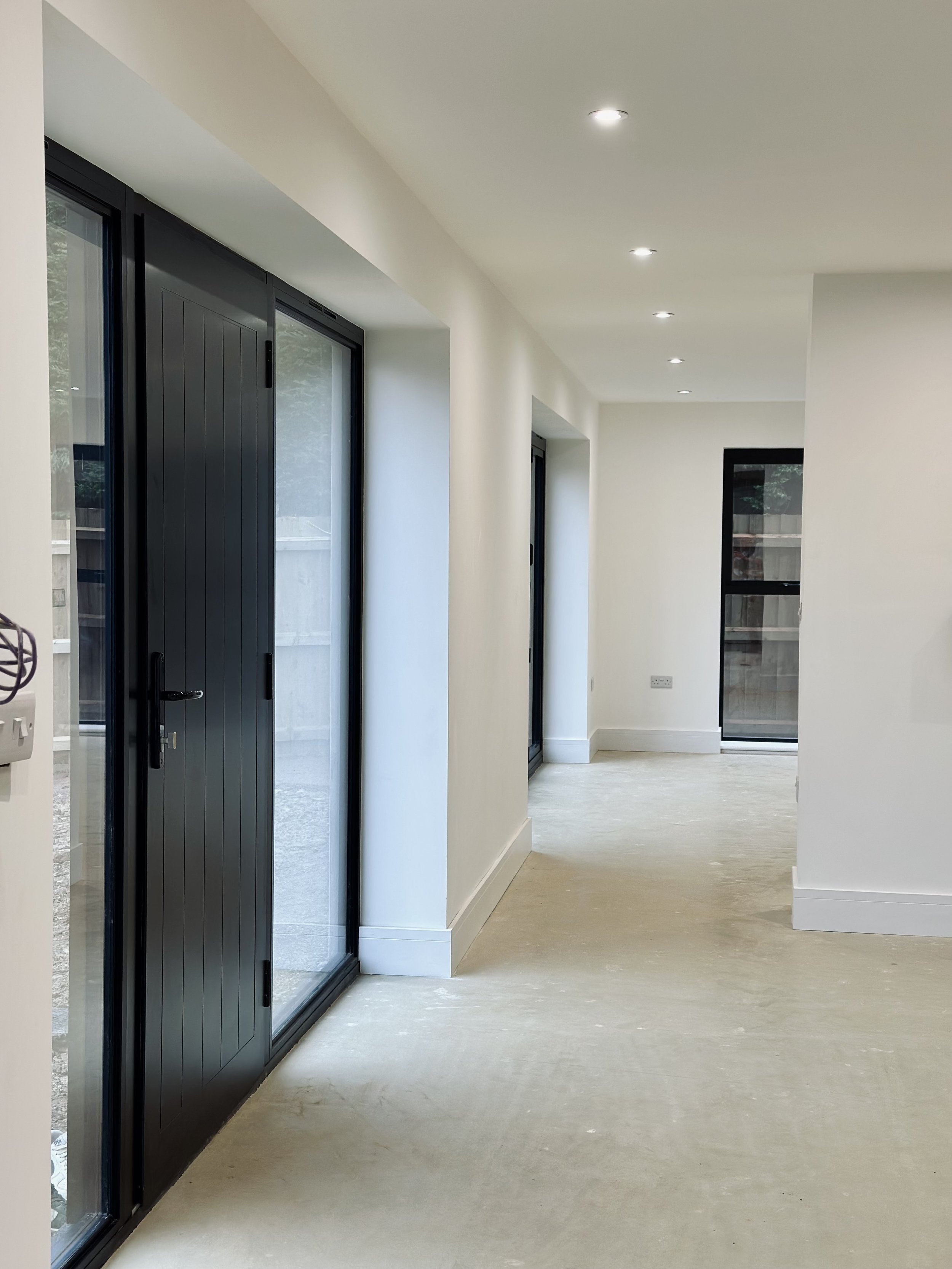 Modern hallway with large sliding glass doors, white walls, recessed ceiling lights, and unfinished floor.