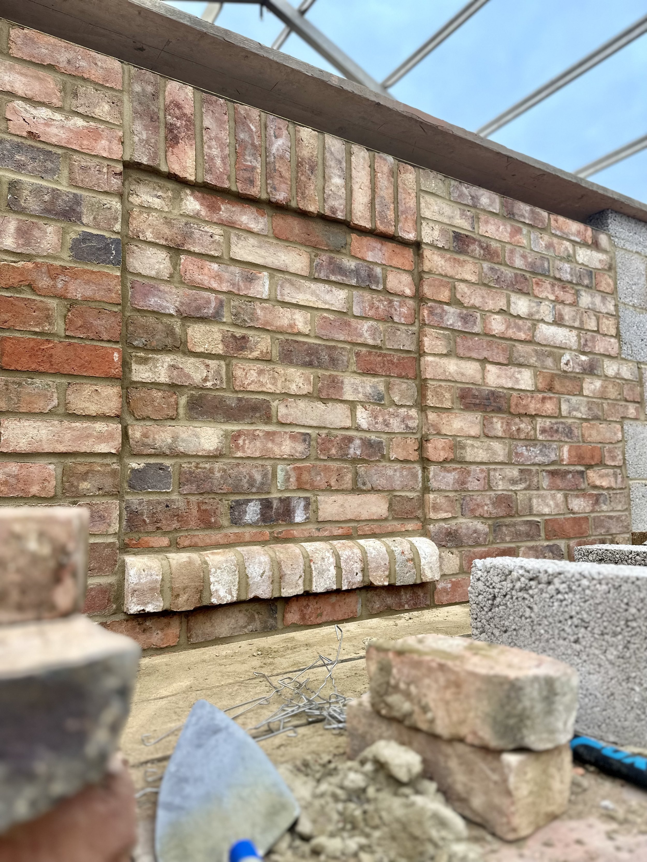 Brick wall under construction with arches, bricks, mortar, and a trowel in the foreground.