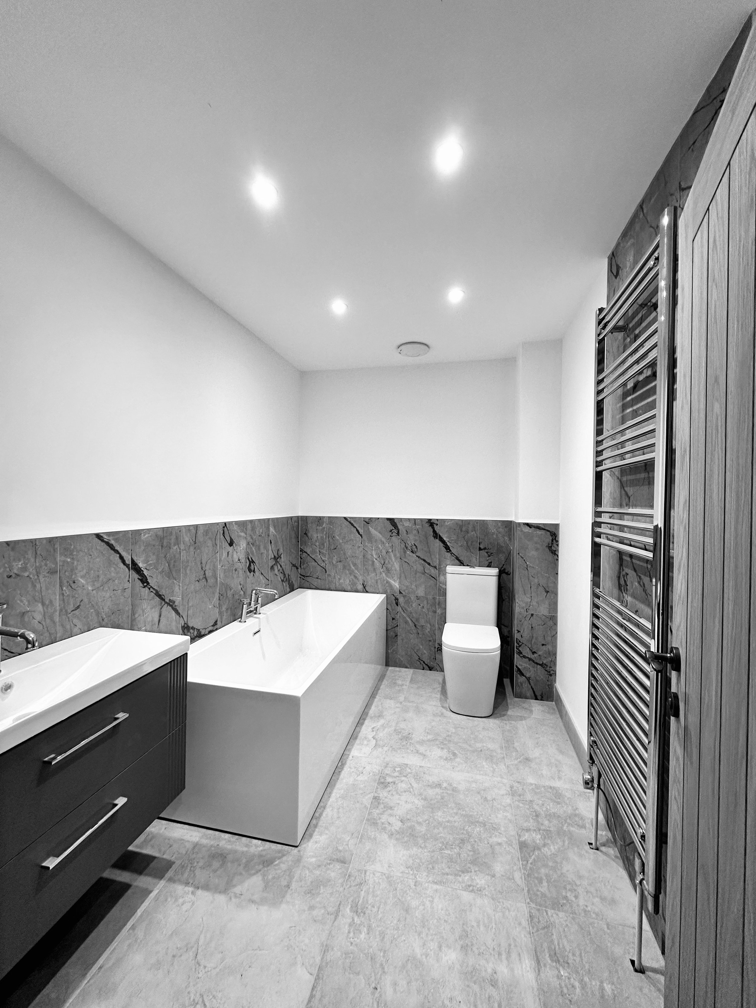 Modern bathroom with bathtub, sink, toilet, and heated towel rail, featuring marble walls and tiled floor.
