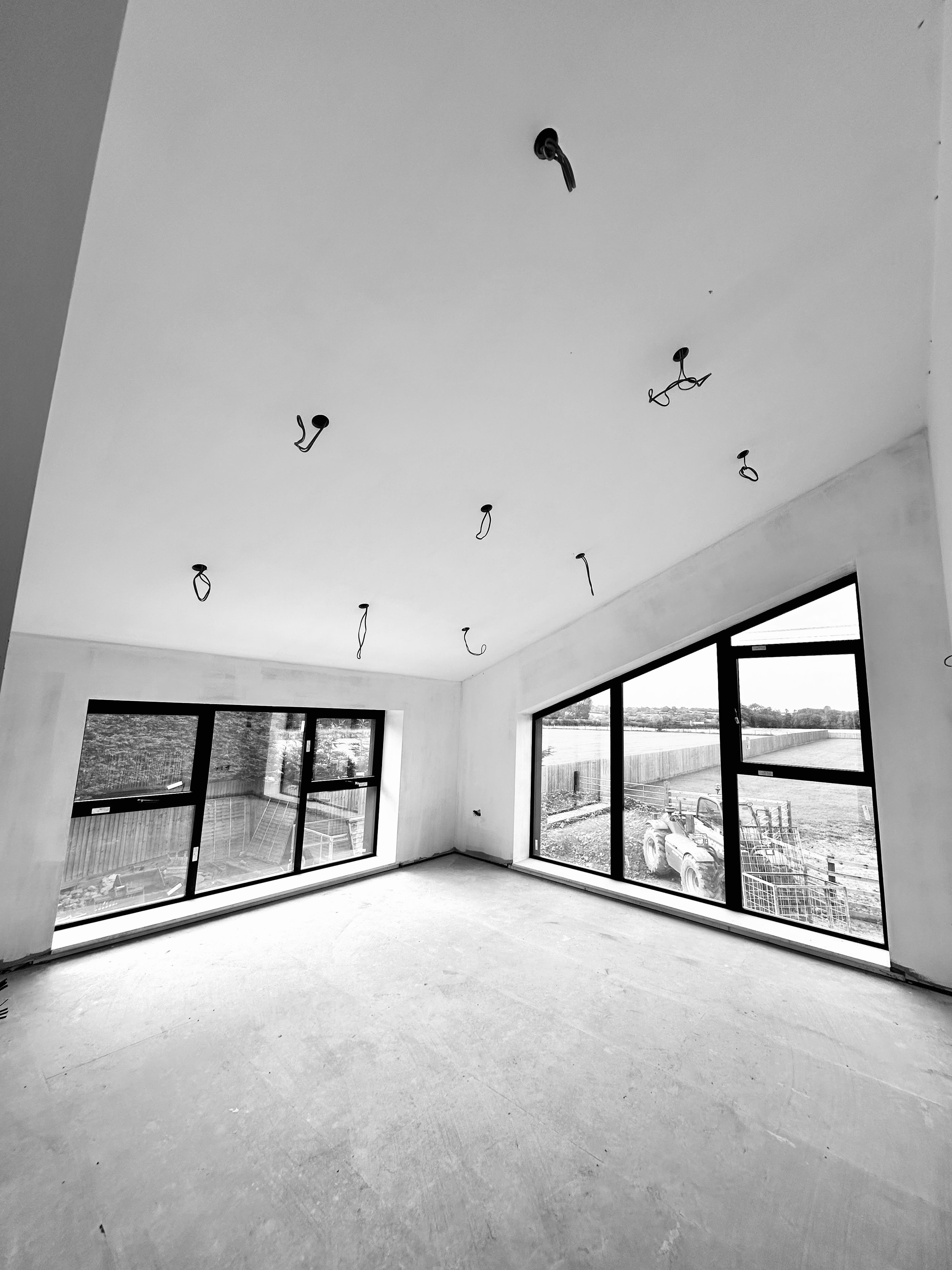 Unfinished interior with large windows, bare floors, and exposed ceiling wiring, overlooking outdoor scenery.