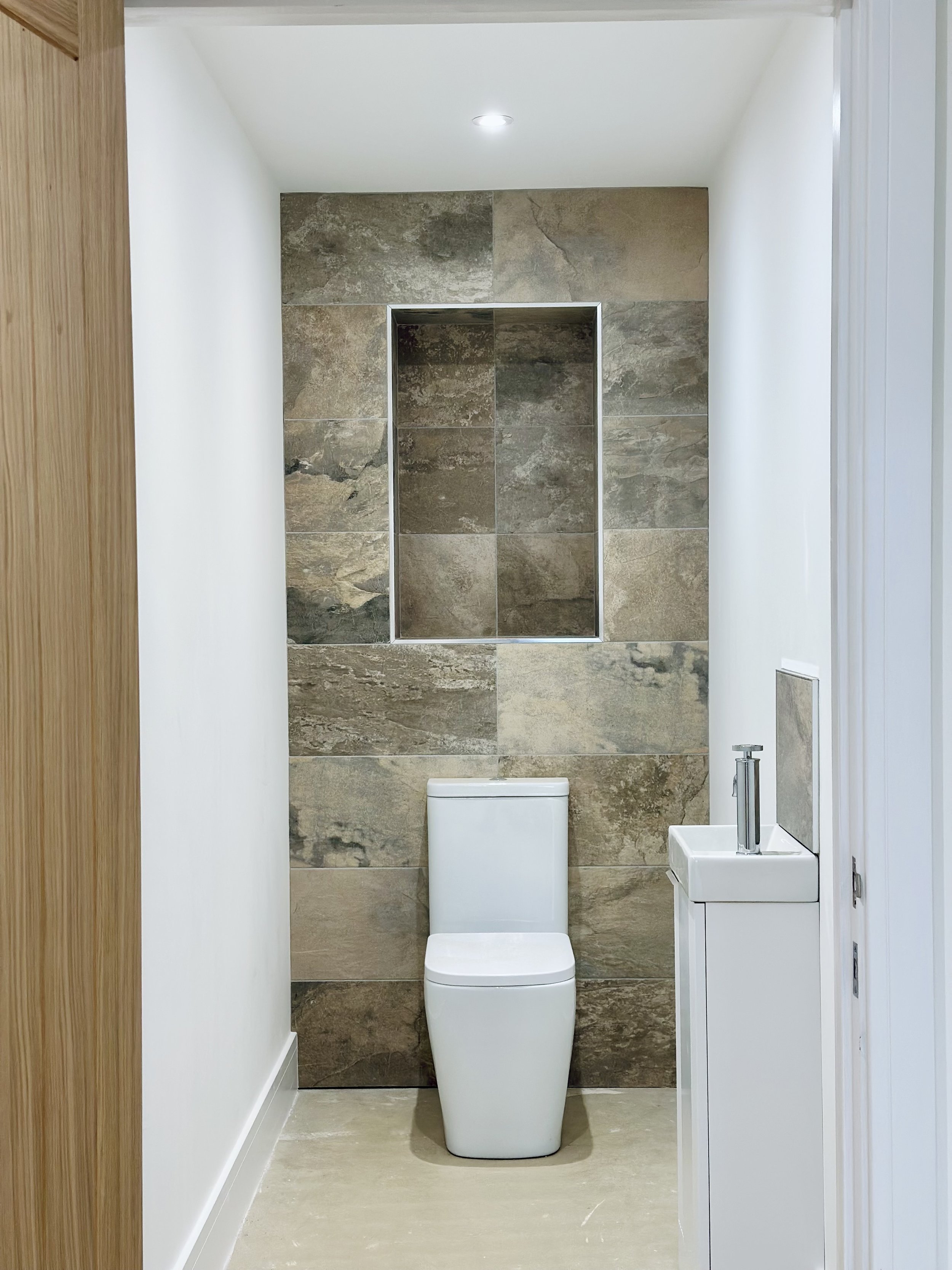 Modern minimalist bathroom with slim toilet, small sink, tile accent wall, and recessed lighting.