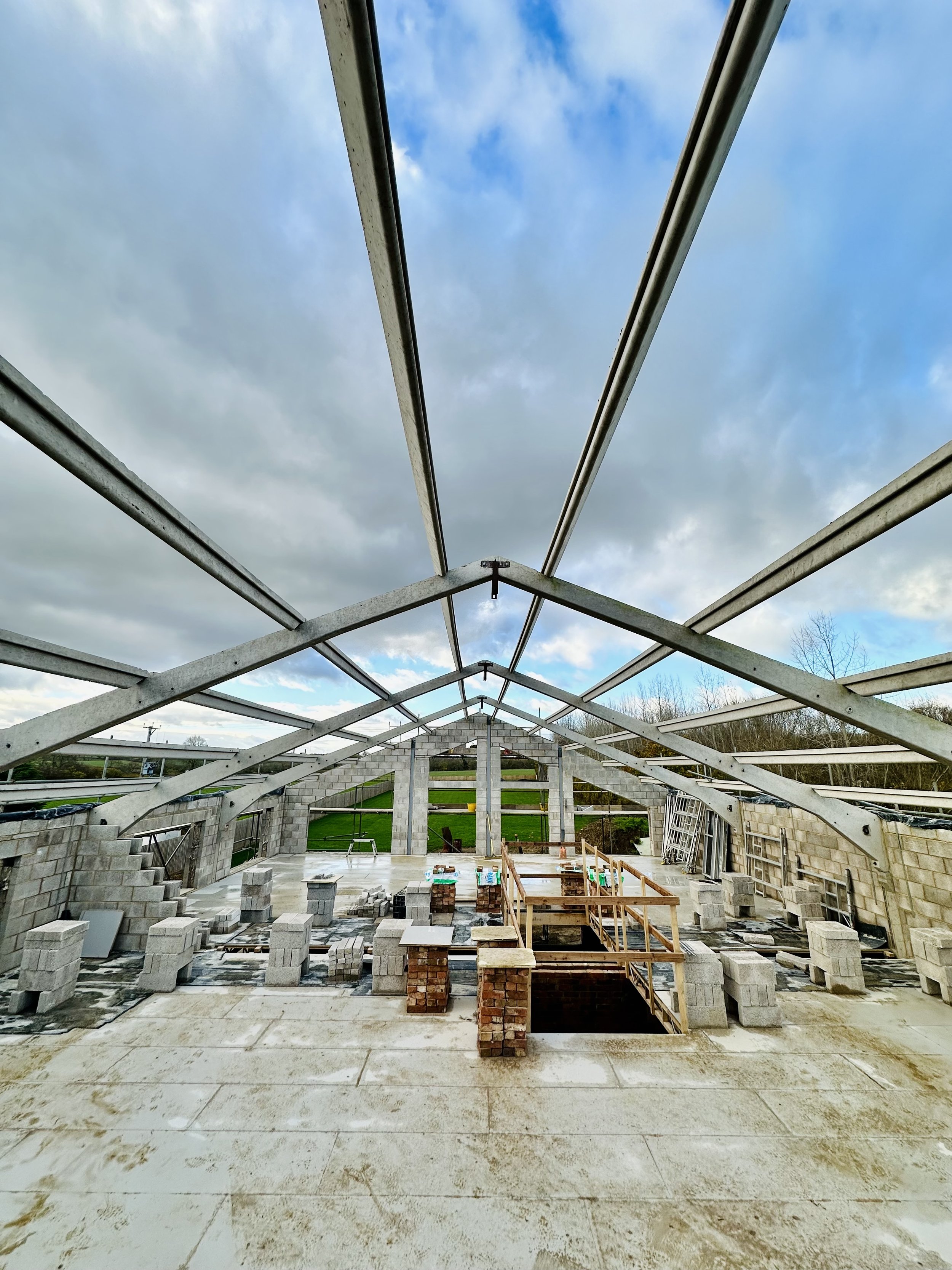 Construction site with incomplete building structure, featuring steel beams and concrete blocks against a cloudy sky.