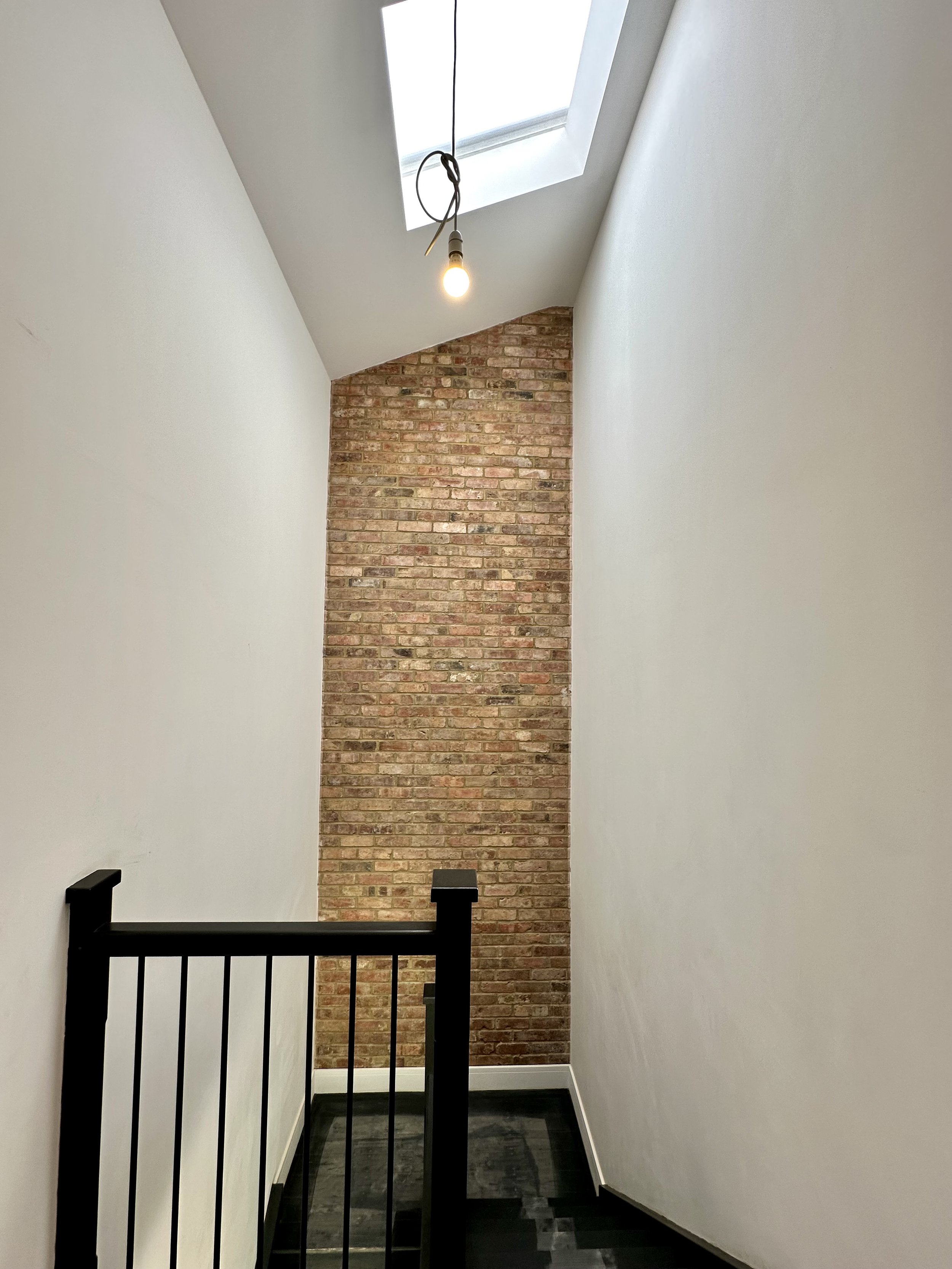 Stairwell with exposed brick wall, skylight, and hanging light bulb.