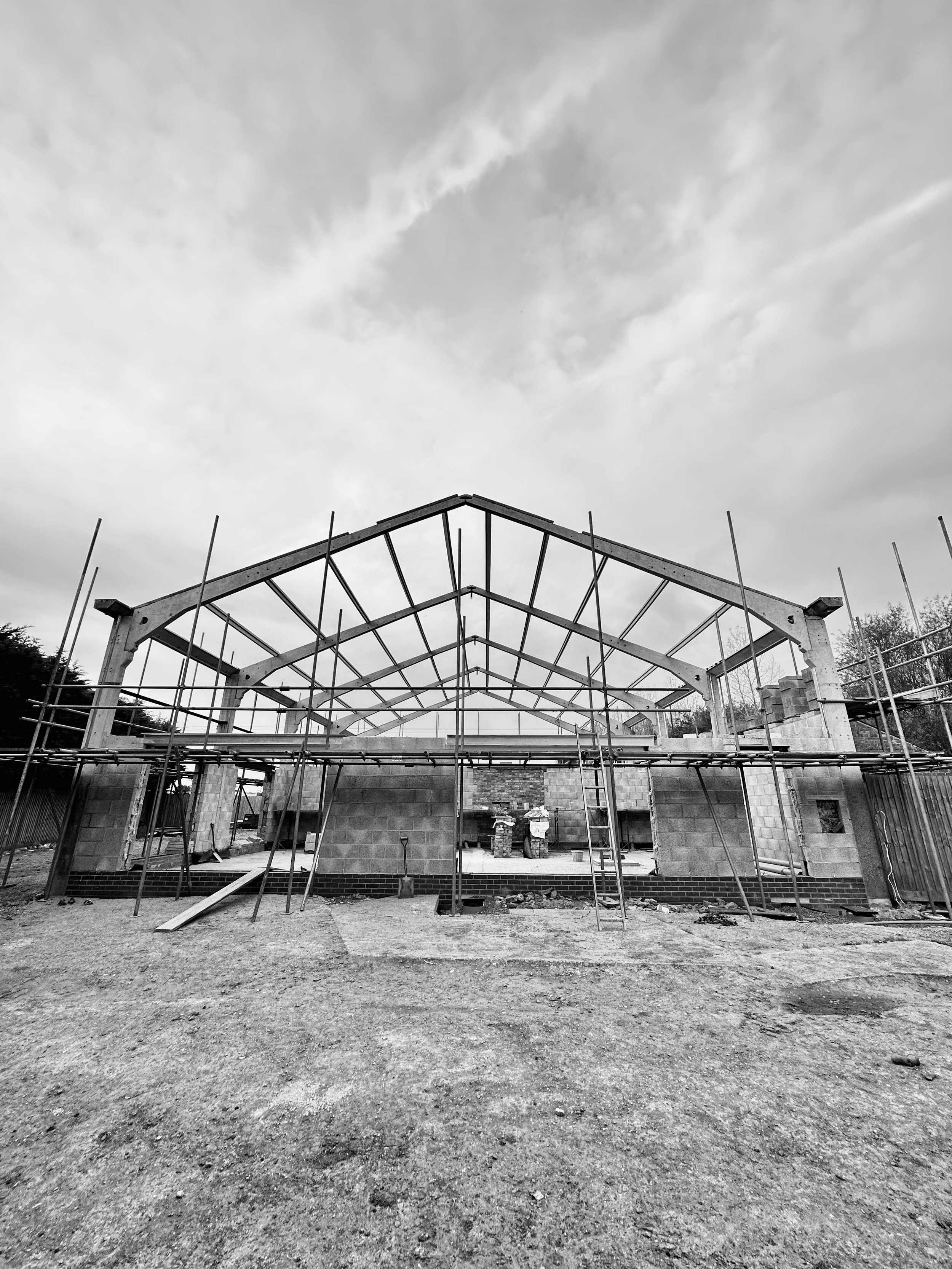 Black and white photo of a partially constructed building frame with scaffolding, concrete walls, and a cloudy sky.