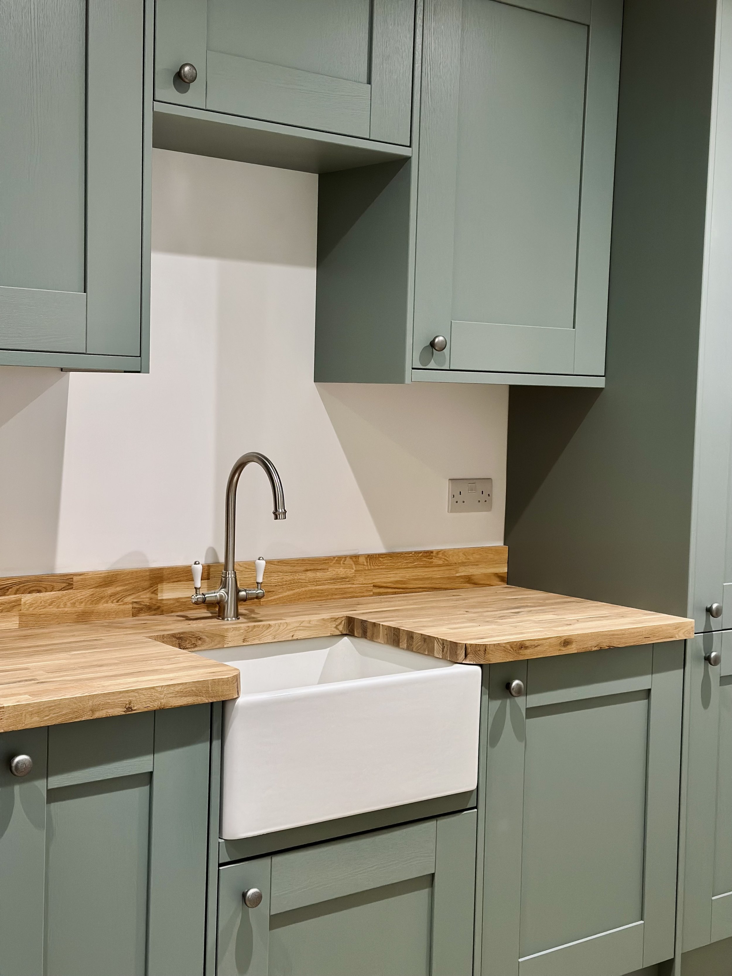 Modern kitchen with green cabinets, wooden countertops, and a white farmhouse sink.