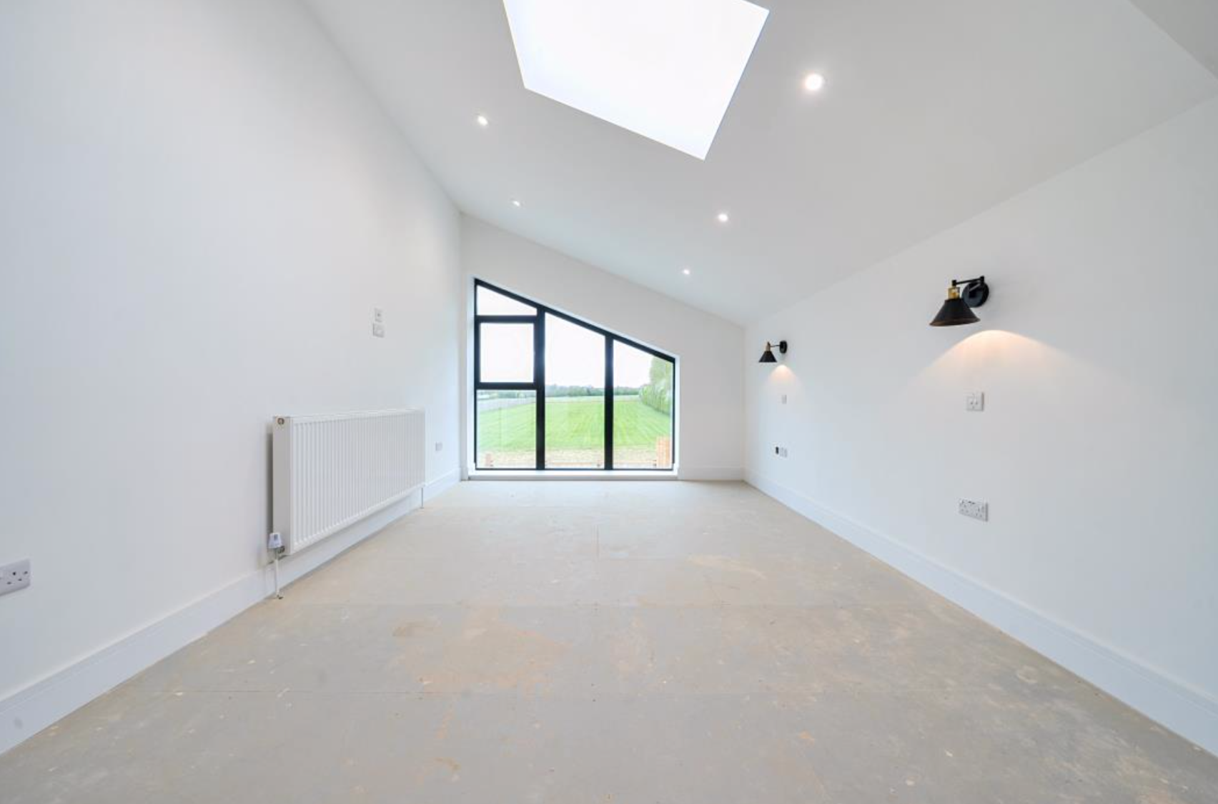 Empty modern room with large window, skylight, wall lamps, and radiator.