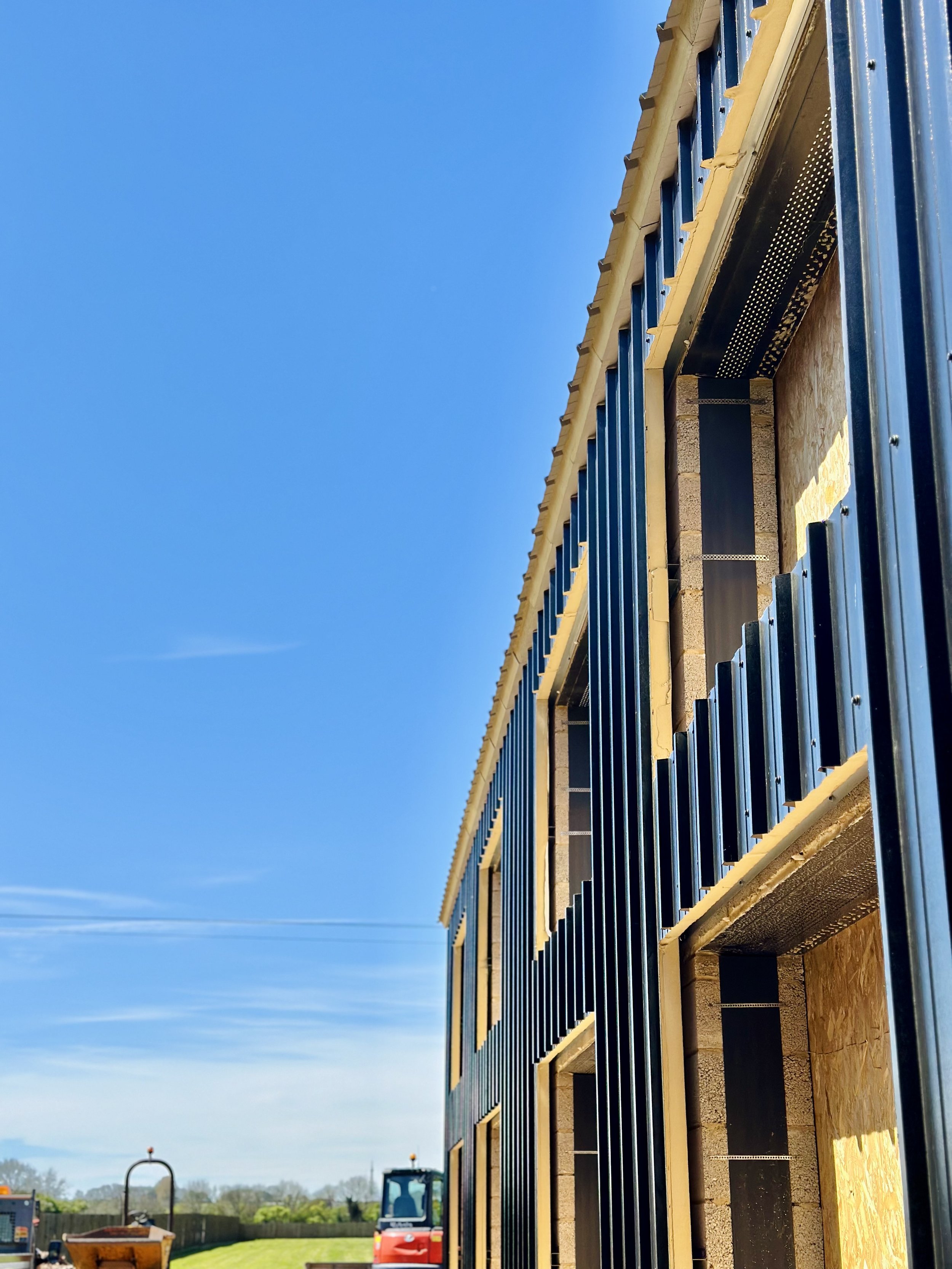 Construction site with partially completed building wall; blue corrugated metal sheets attached, clear sky background.