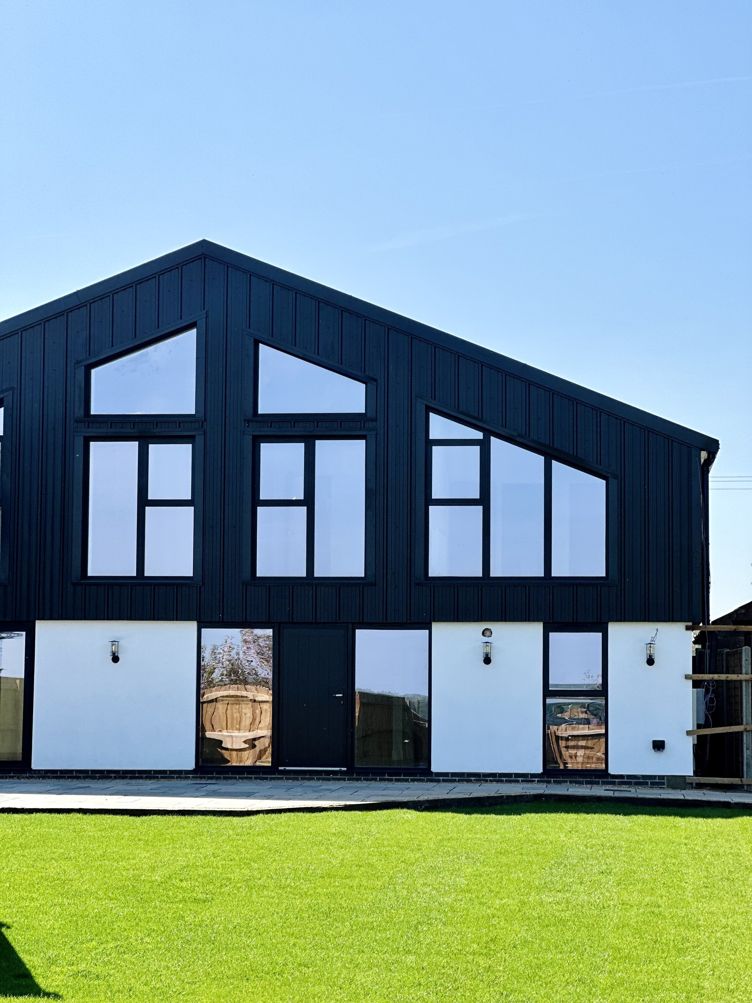 Modern house exterior with black and white paneling, large windows, and a sloped roof, set against a clear blue sky and manicured lawn.