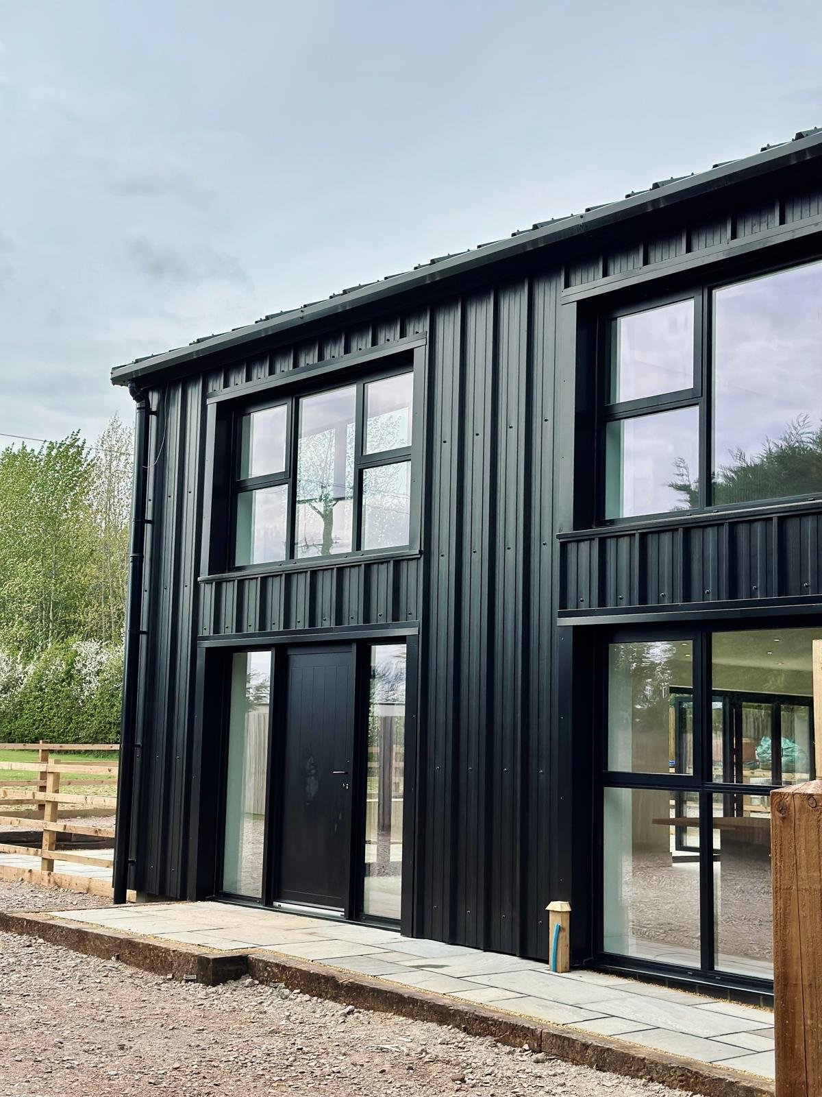 Modern black metal building with large windows and glass door; surrounded by natural landscape.
