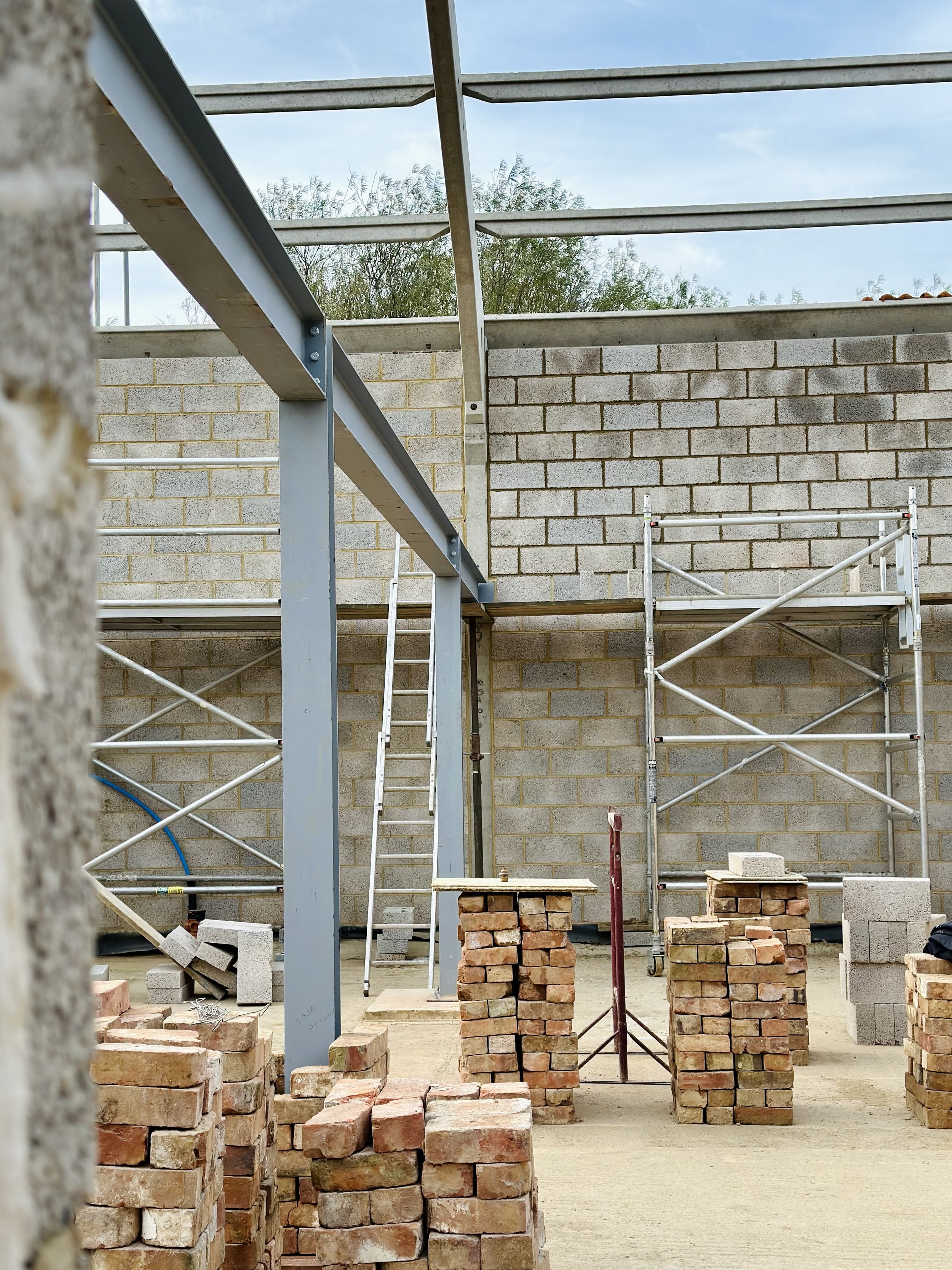 Building construction site with steel beams, brick walls, stacks of bricks, scaffolding, and a ladder.