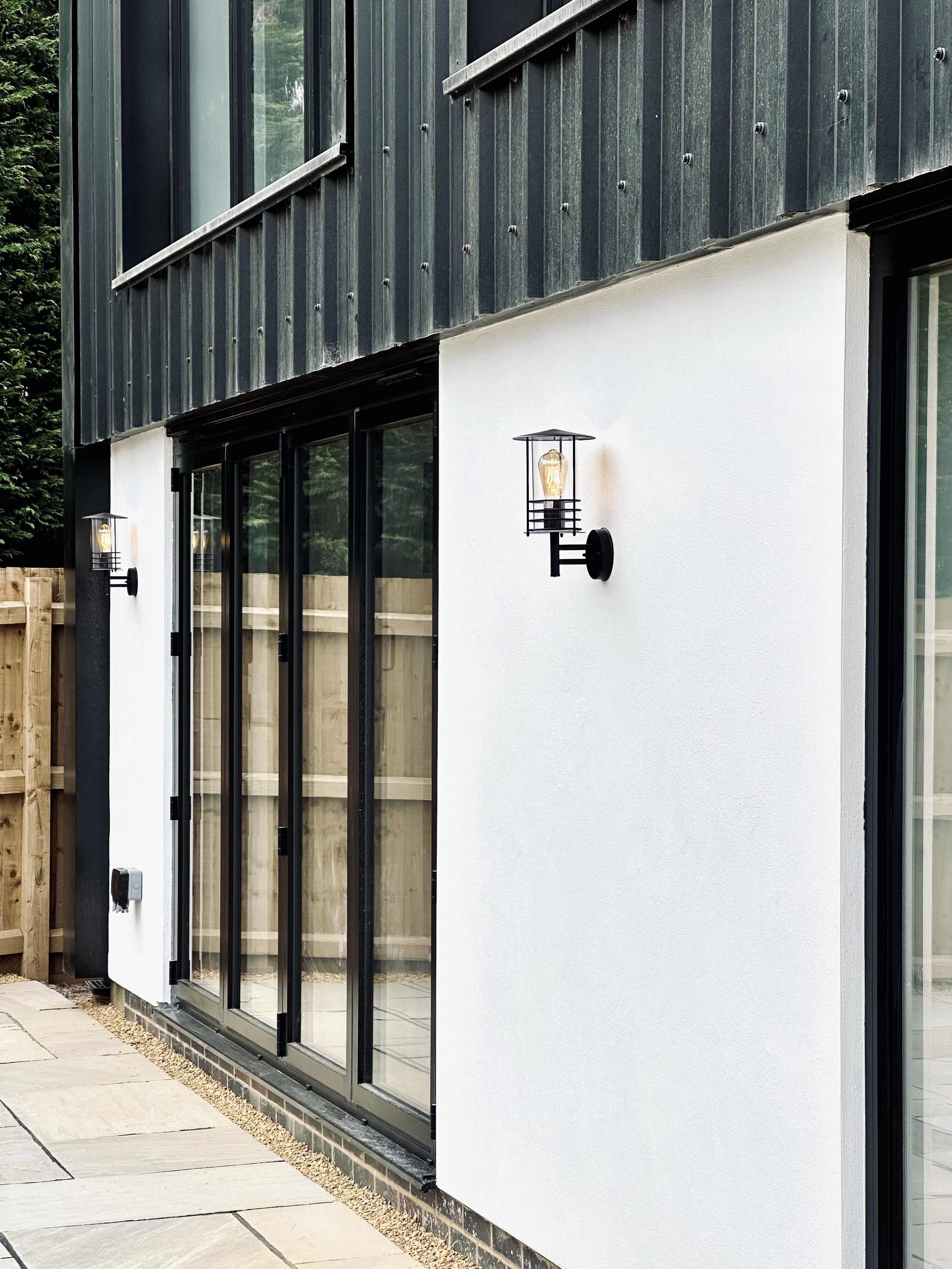 Modern building exterior with large glass doors, white stucco walls, and black wall-mounted outdoor lights.