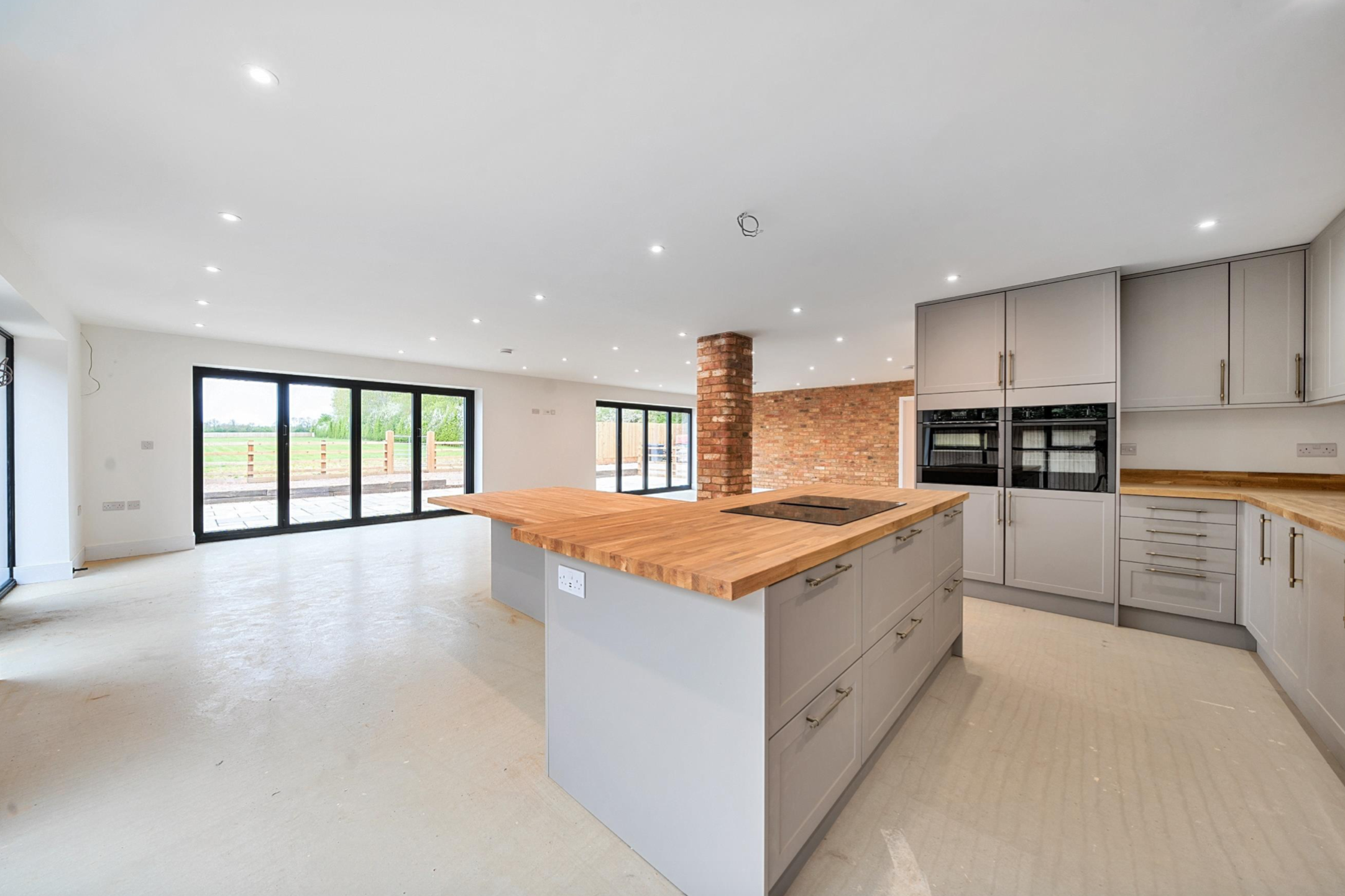 Modern kitchen with large island, wood countertops, brick accent wall, and sliding glass doors.