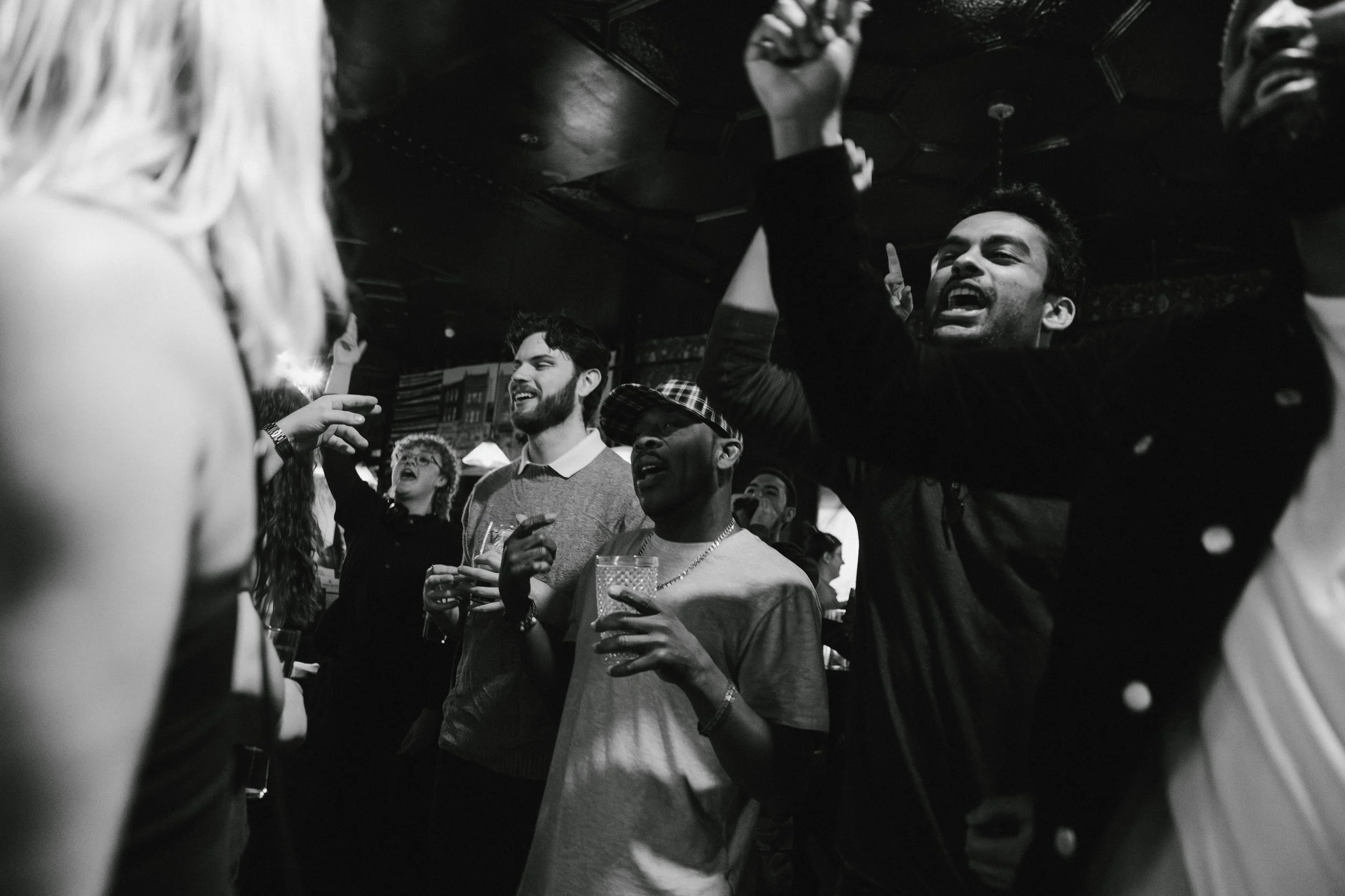 A group of young people gathered in a bar or club, engaged in lively conversation and laughter, with some holding drinks.